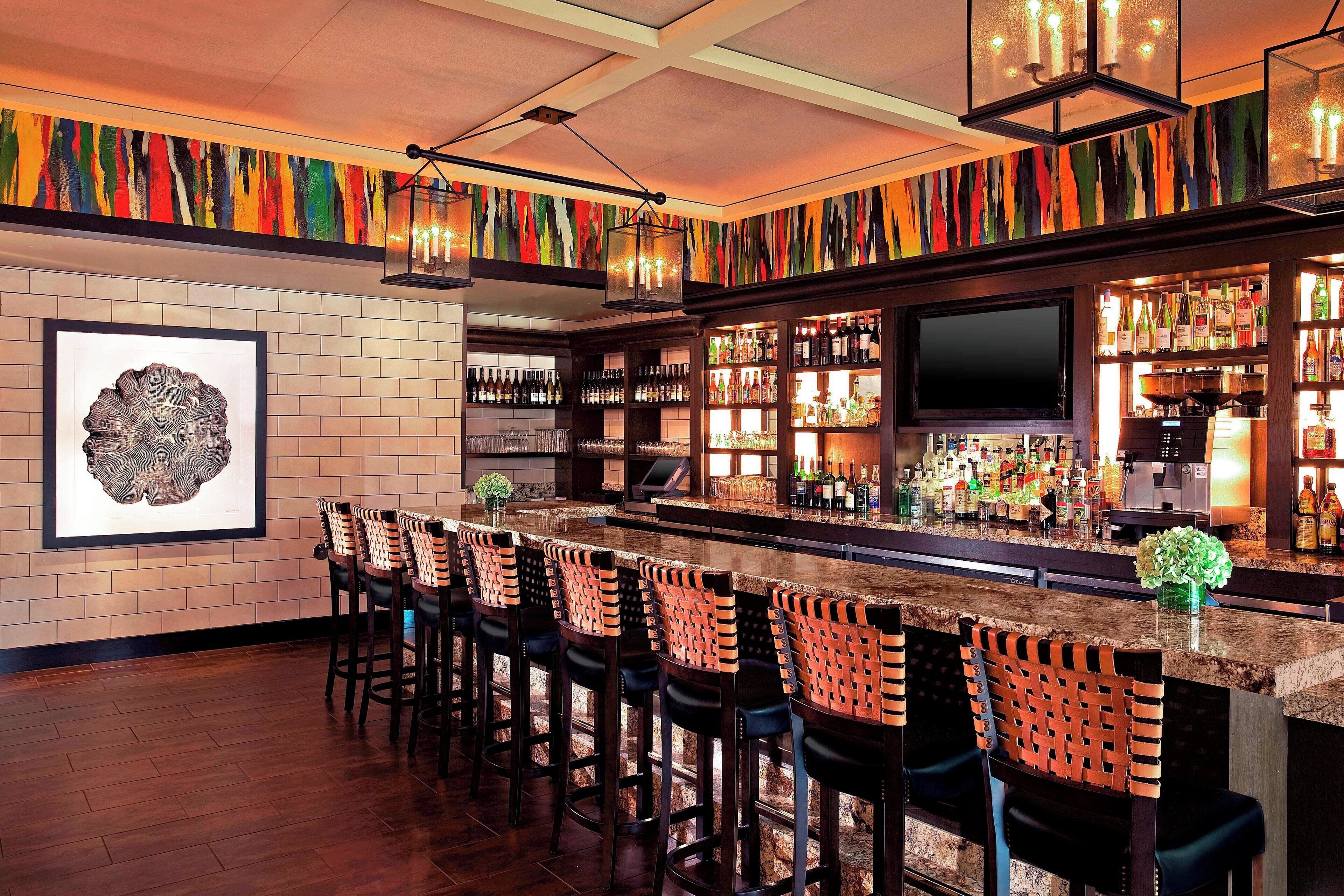A bar area with a long counter, multiple bar stools, and a variety of bottles and glasses.