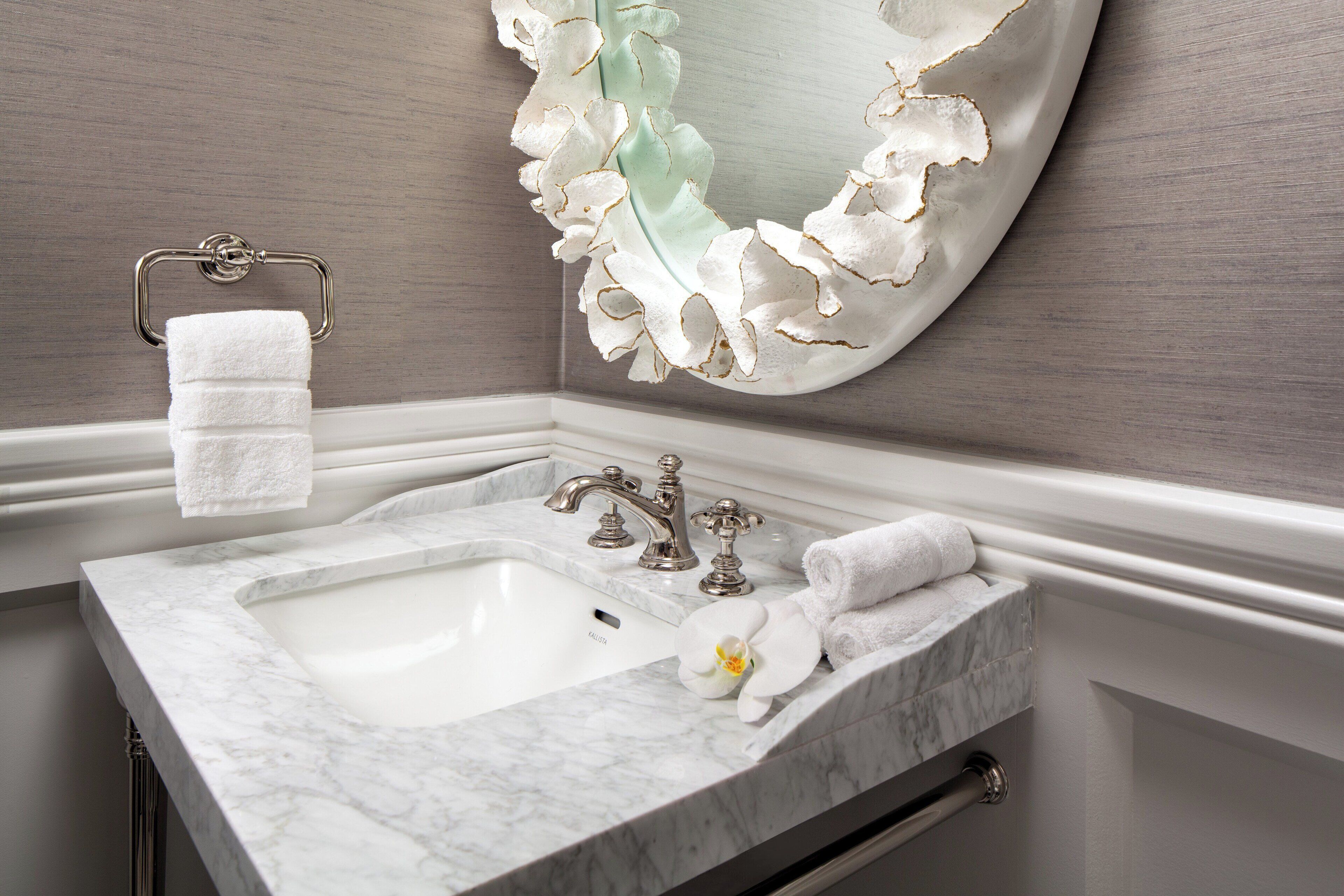A bathroom with a marble sink, two faucets, a towel rack, and a decorative mirror.