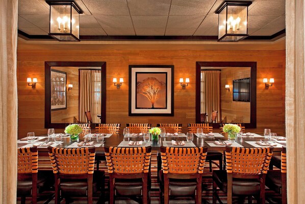 A formal dining room with wooden walls, framed artwork, and modern lighting fixtures.