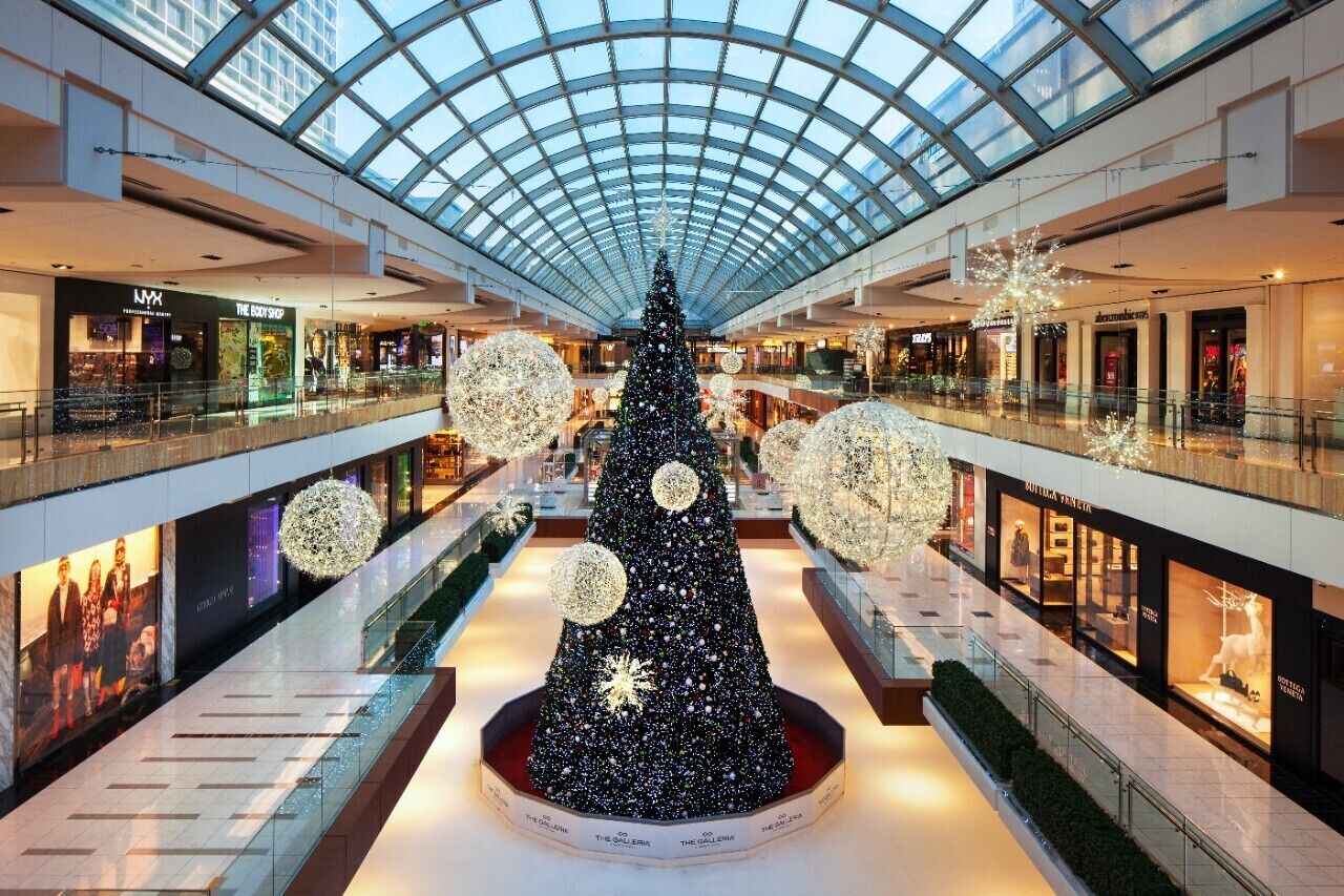A shopping mall with a large Christmas tree in the center, surrounded by illuminated spherical decorations.