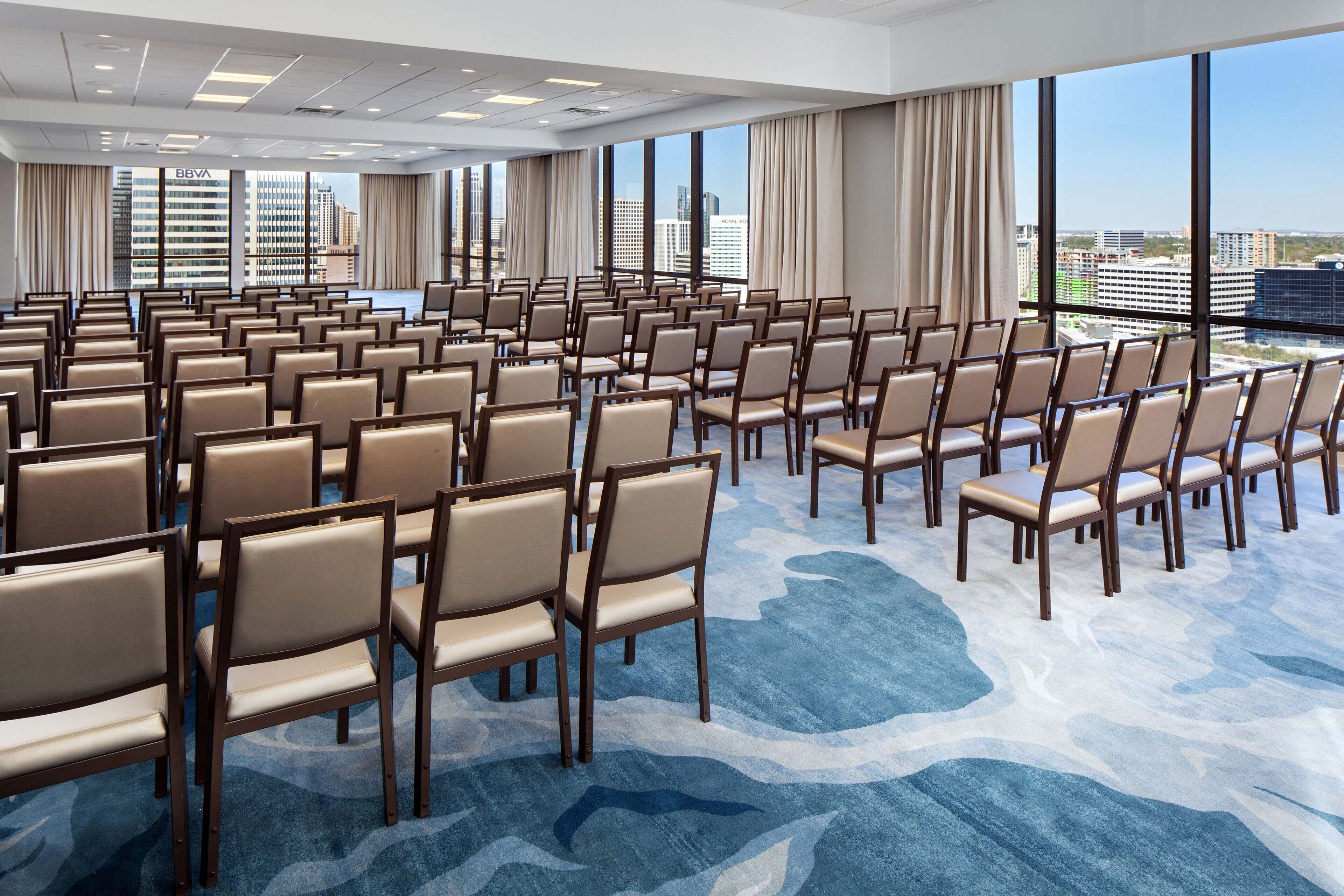 A conference room with rows of chairs and large windows offering a city view.