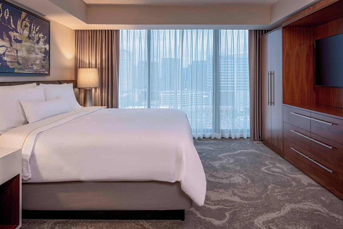Een hotelkamer met een groot bed, een televisie, een kledingkast en uitzicht op de stad.