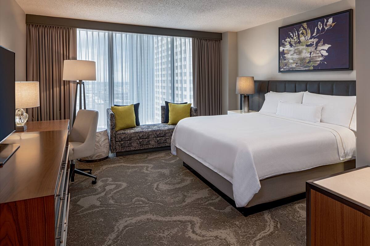 Een hotelkamer met een groot bed, een bureau, een stoel en een raam met gordijnen.