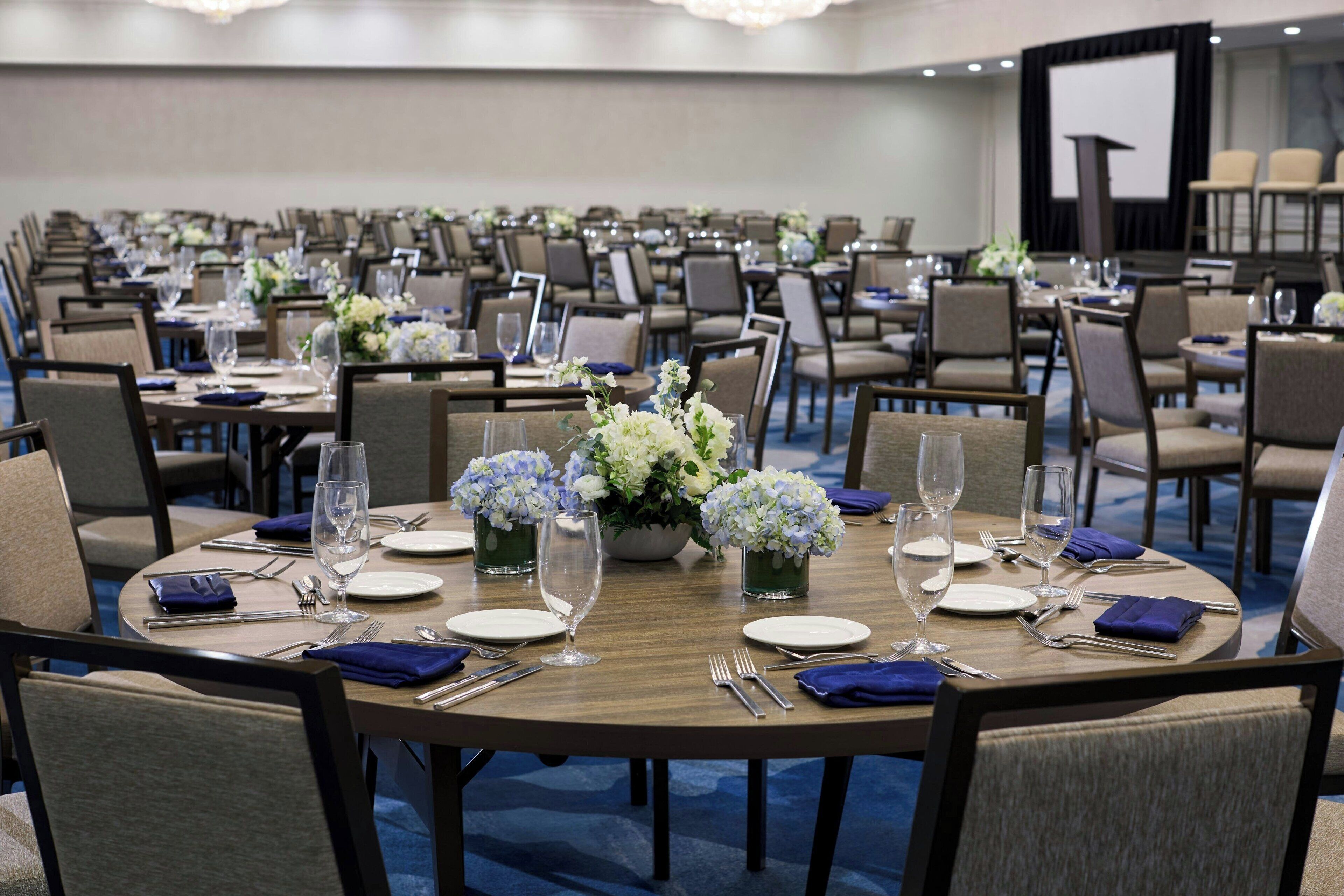 A conference room with round tables set for dining, equipped with chairs, plates, cutlery, and glassware.