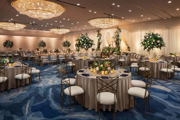 Une salle de banquet avec des tables rondes, des chaises blanches et des lustres.
