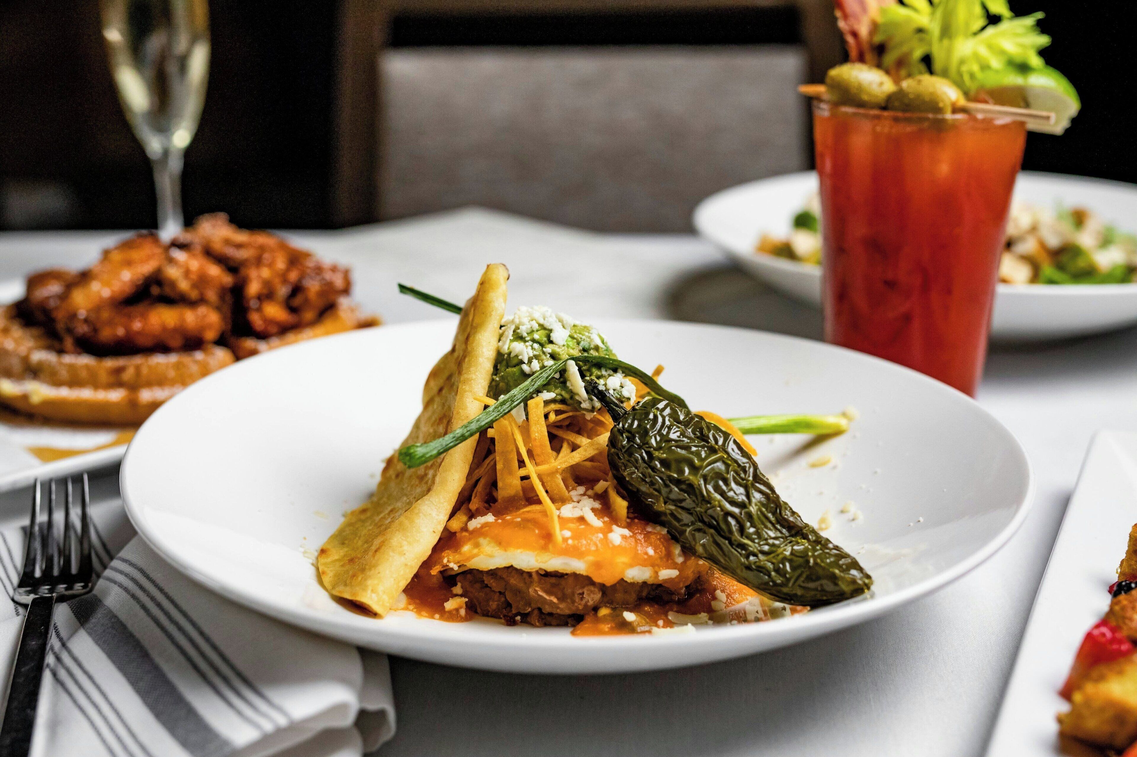 A plate of food with a stuffed pepper, a glass of red drink, and a fork on a table.