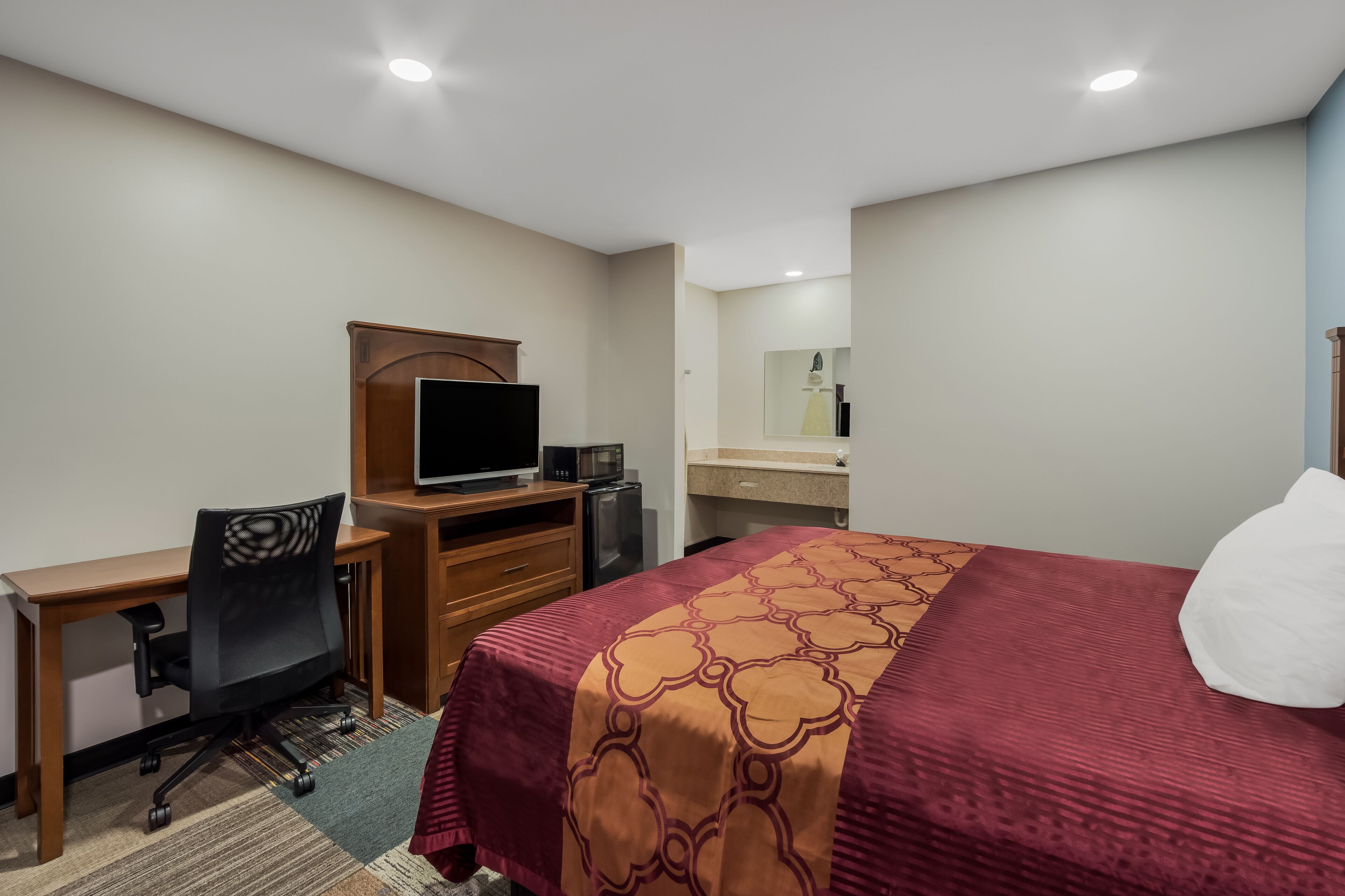 A hotel room with a bed, a desk with a computer, a chair, a television, and a small kitchenette.