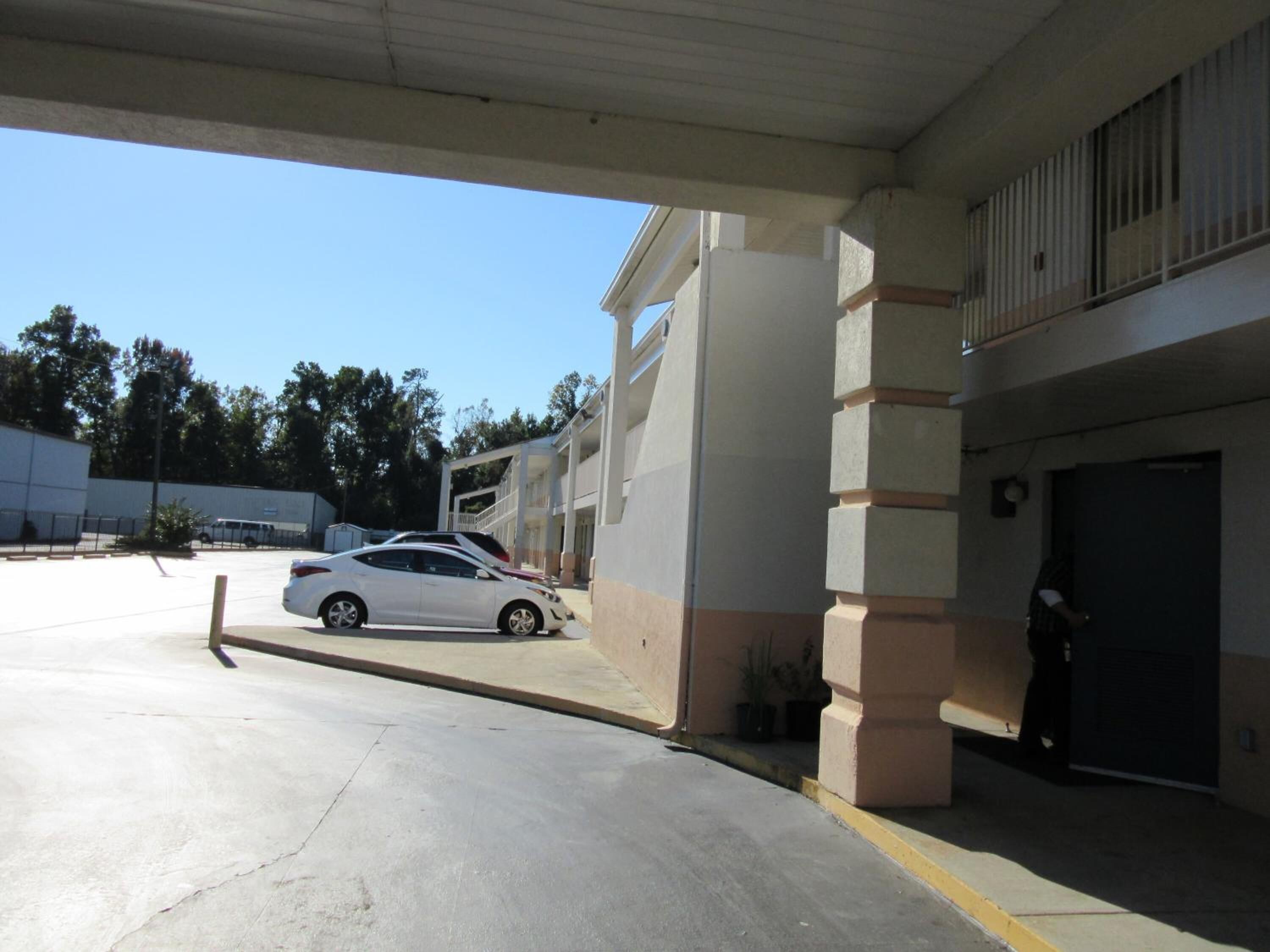 Un área de estacionamiento con un coche blanco aparcado bajo una estructura cubierta.