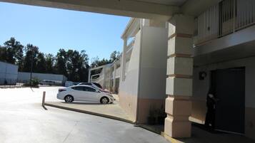 Un área de estacionamiento con un coche blanco aparcado bajo una estructura cubierta.