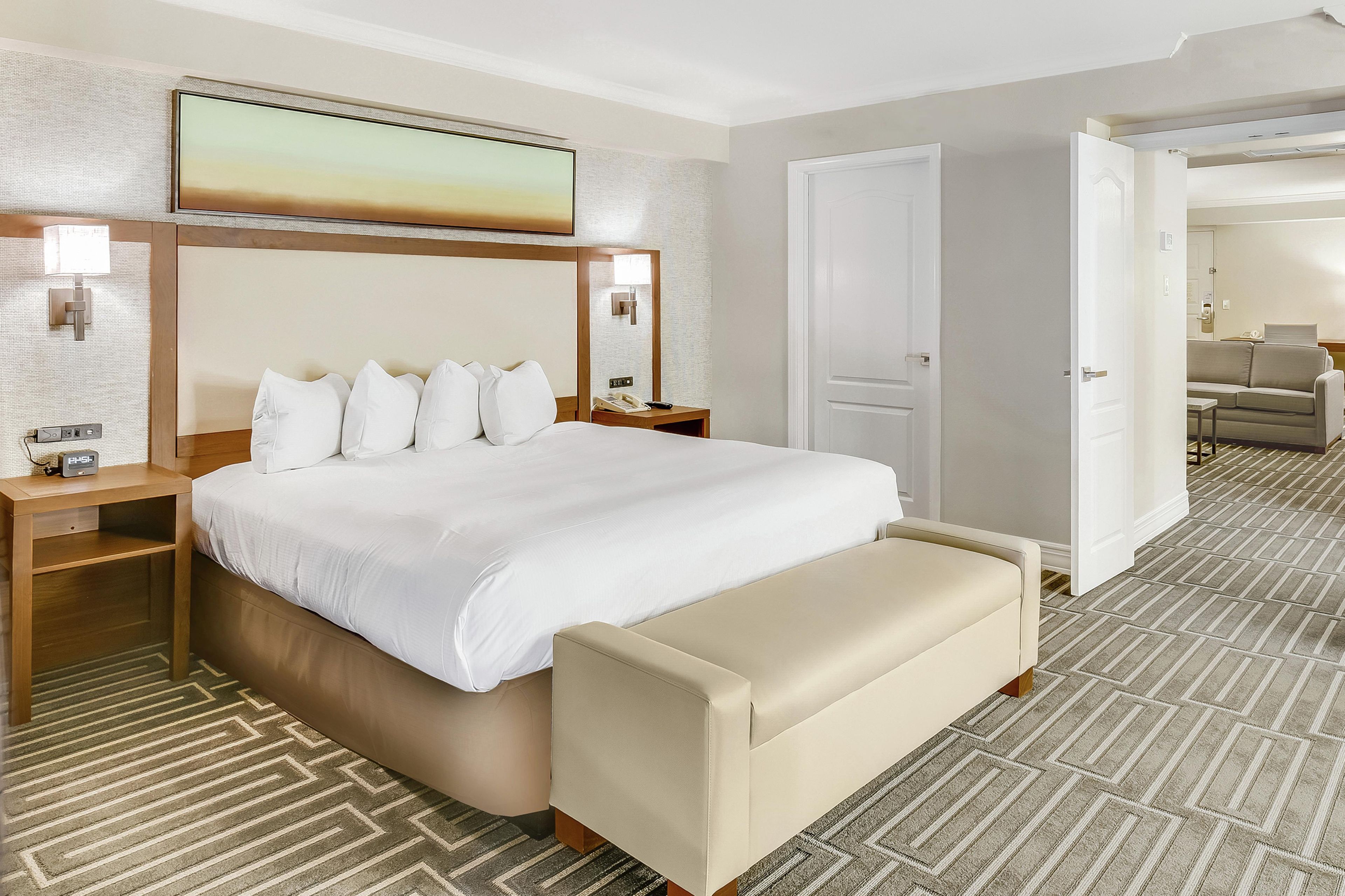 Une chambre d’hôtel avec un grand lit, des tables de chevet, un banc, un tableau et une moquette à motifs.