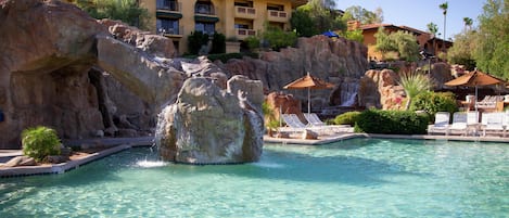 A pool with a rock waterfall, lounge chairs, and a building with balconies.