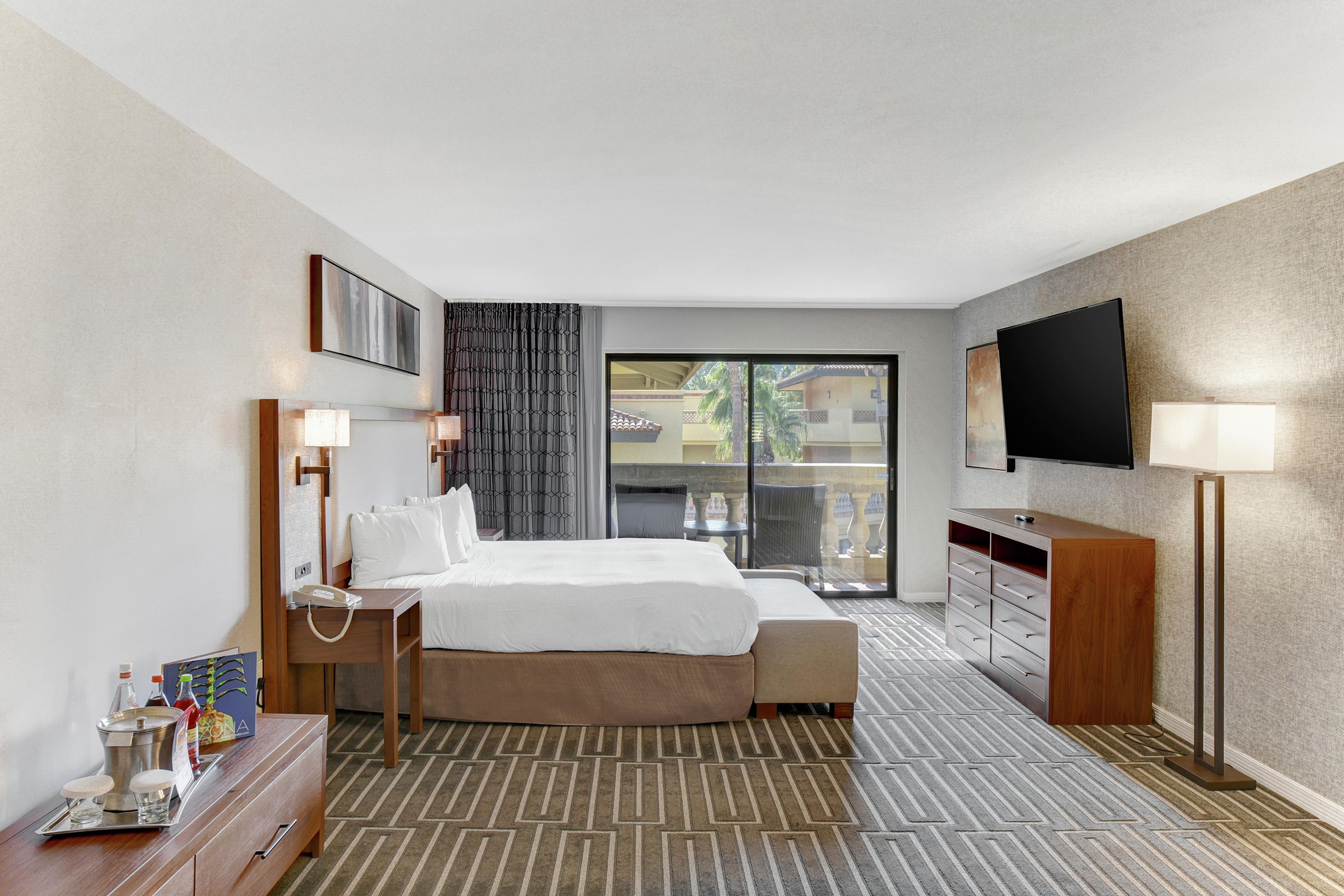 Ein Hotelzimmer mit Bett, Nachttisch, Lampe, Fernseher und Blick aus dem Fenster.