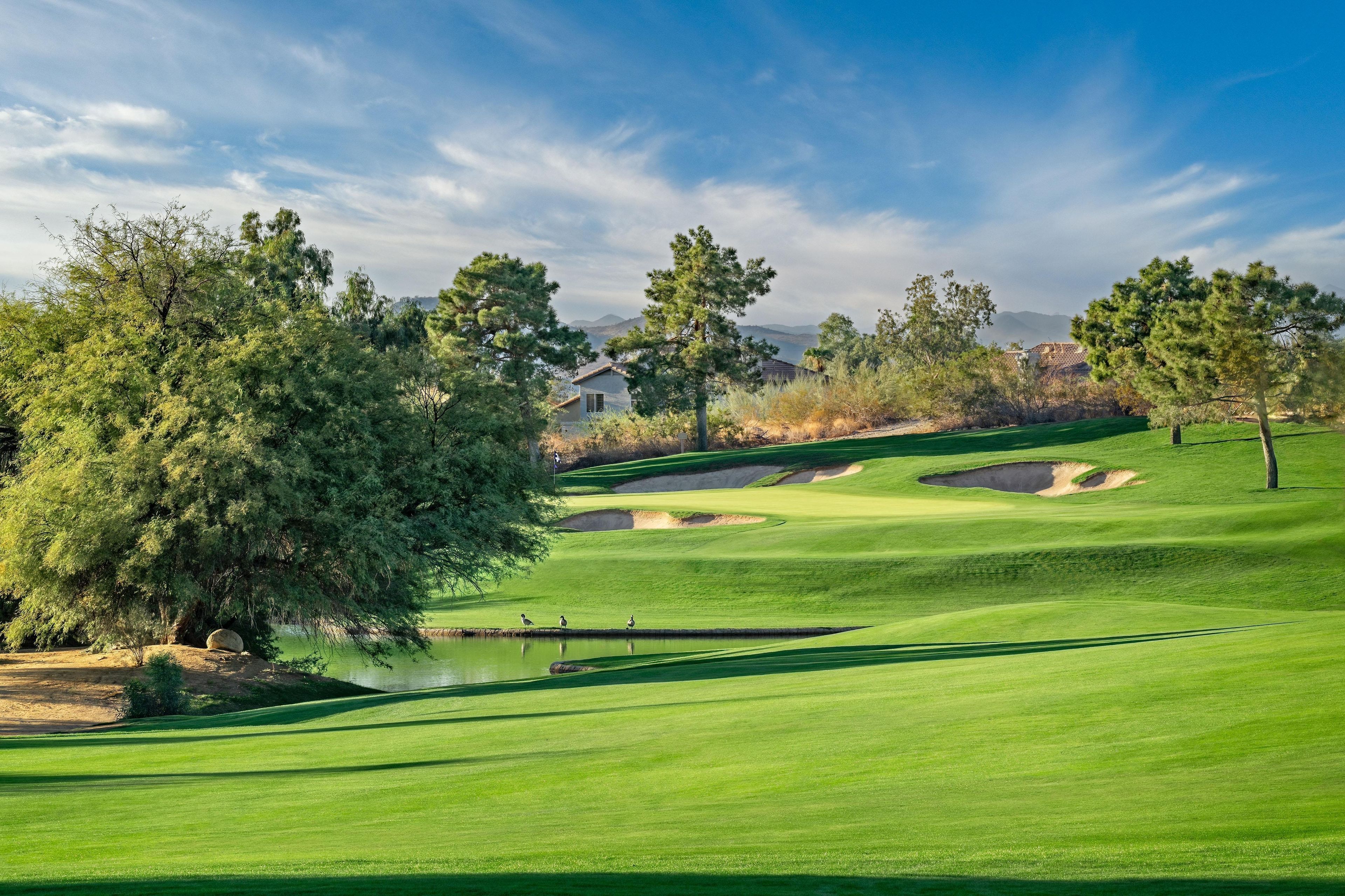 Un terrain de golf avec un étang, des arbres et une maison en arrière-plan.