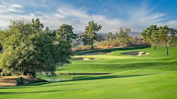 Un terrain de golf avec un étang, des arbres et une maison en arrière-plan.