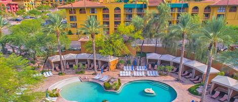 A resort with a large pool, sun loungers, and a mountainous backdrop.