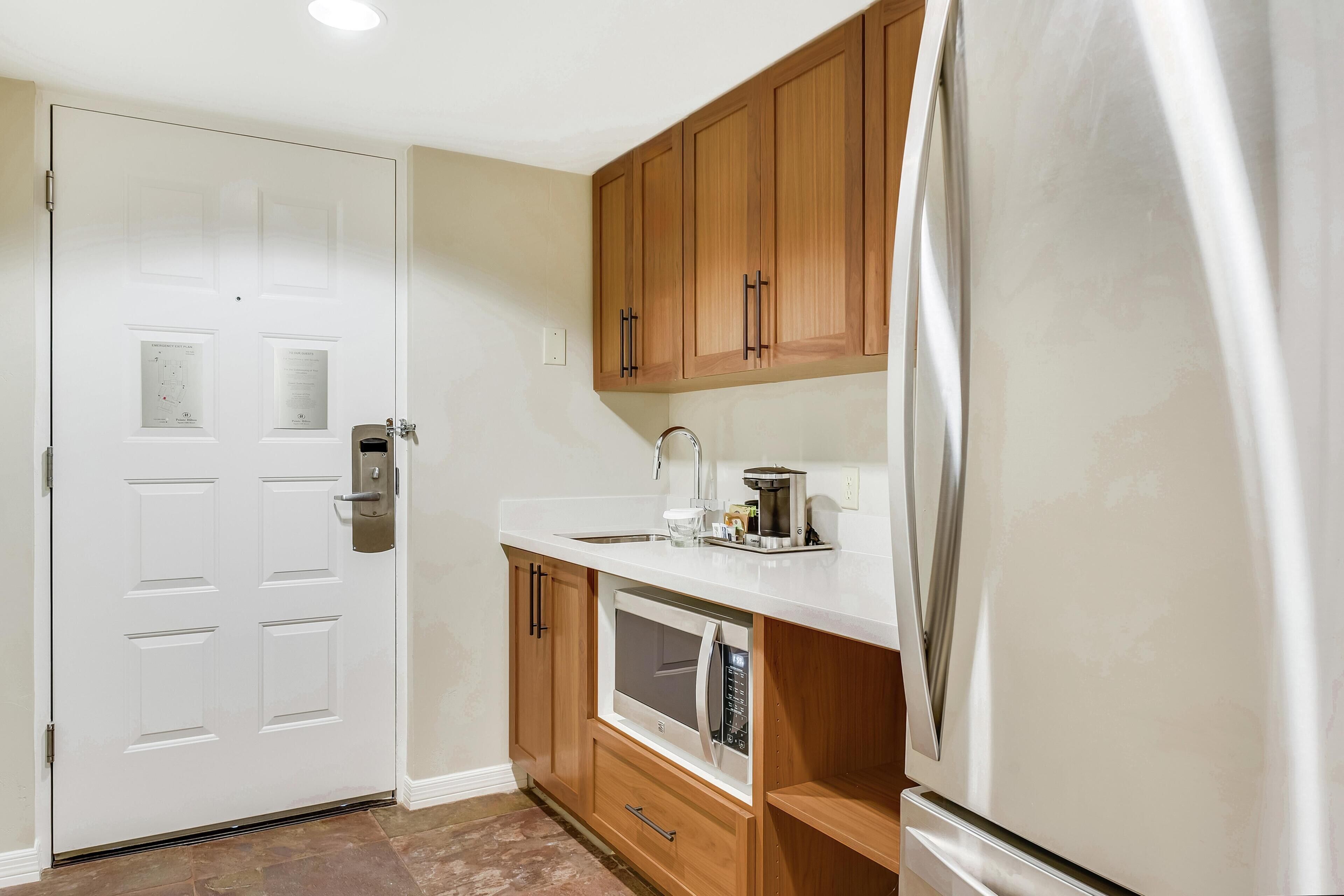 Una cocina con armarios de madera, encimera blanca, refrigerador de acero inoxidable y microondas.