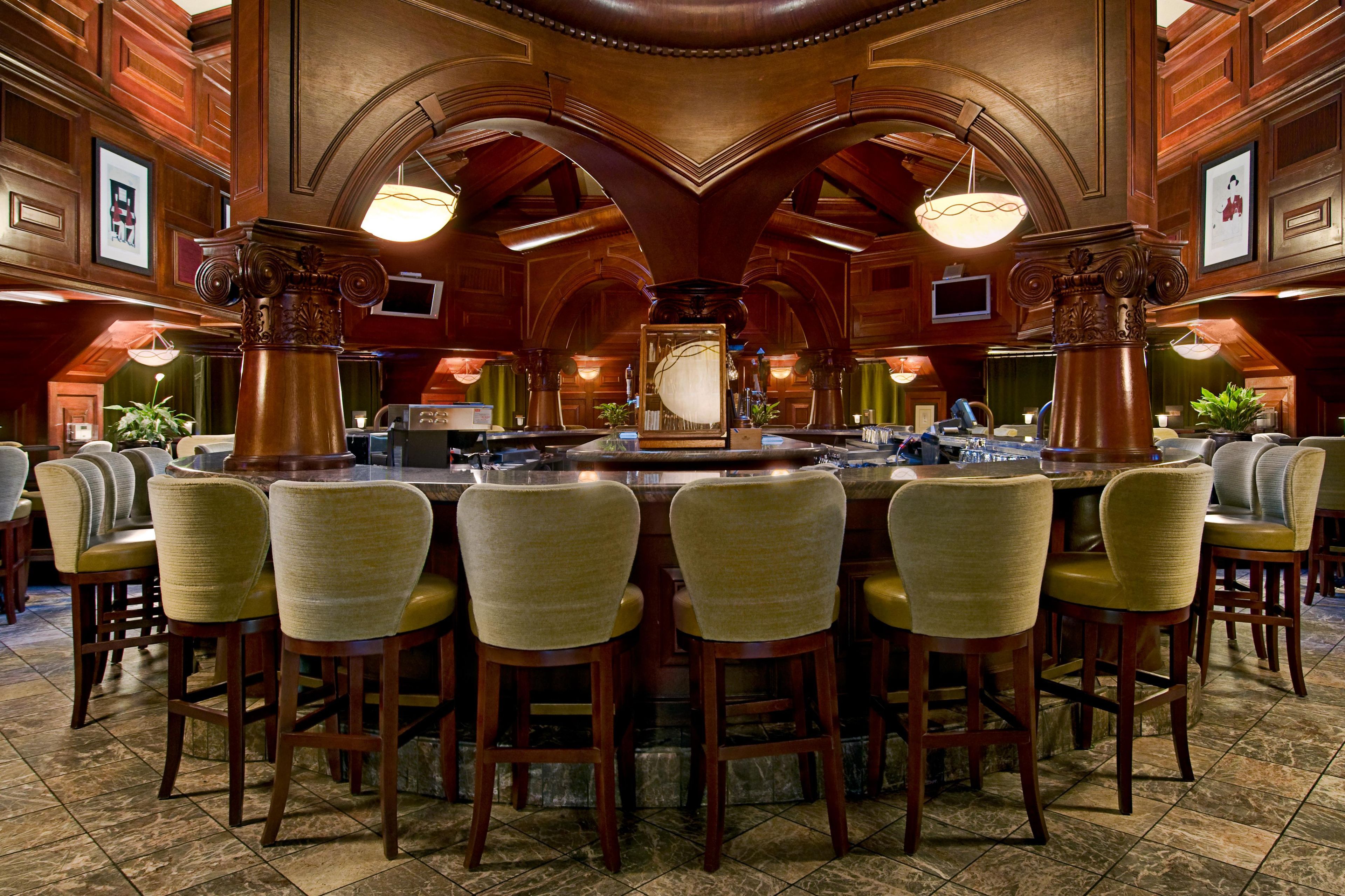 A bar area with a central bar counter, multiple bar stools, and a high ceiling with decorative woodwork.