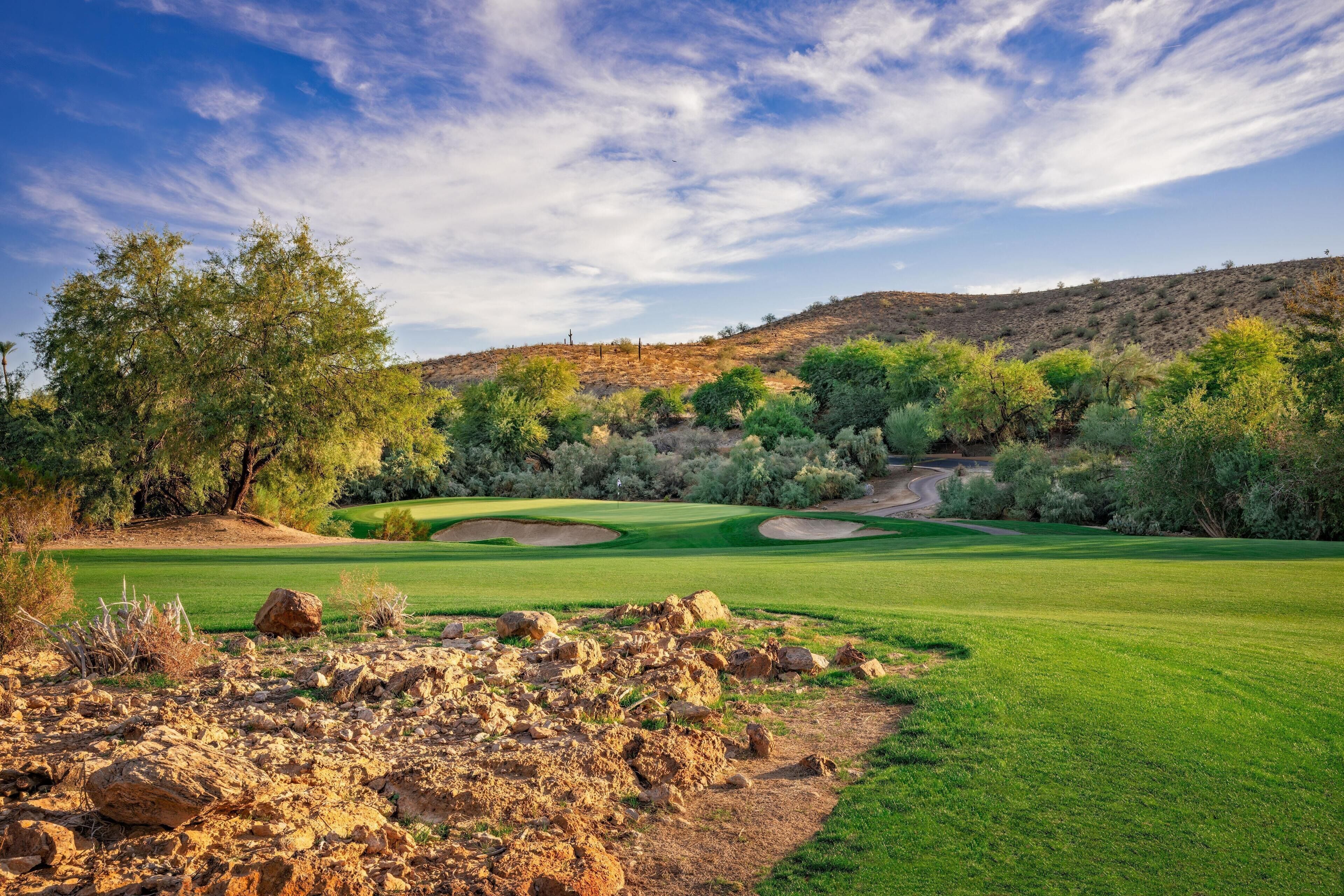 A golf course with a clear sky, green grass, and rocky terrain.
