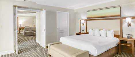 Quarto de hotel com uma cama, um banco, uma mesa de cabeceira, uma televisão fixada na parede e uma porta para outro quarto.