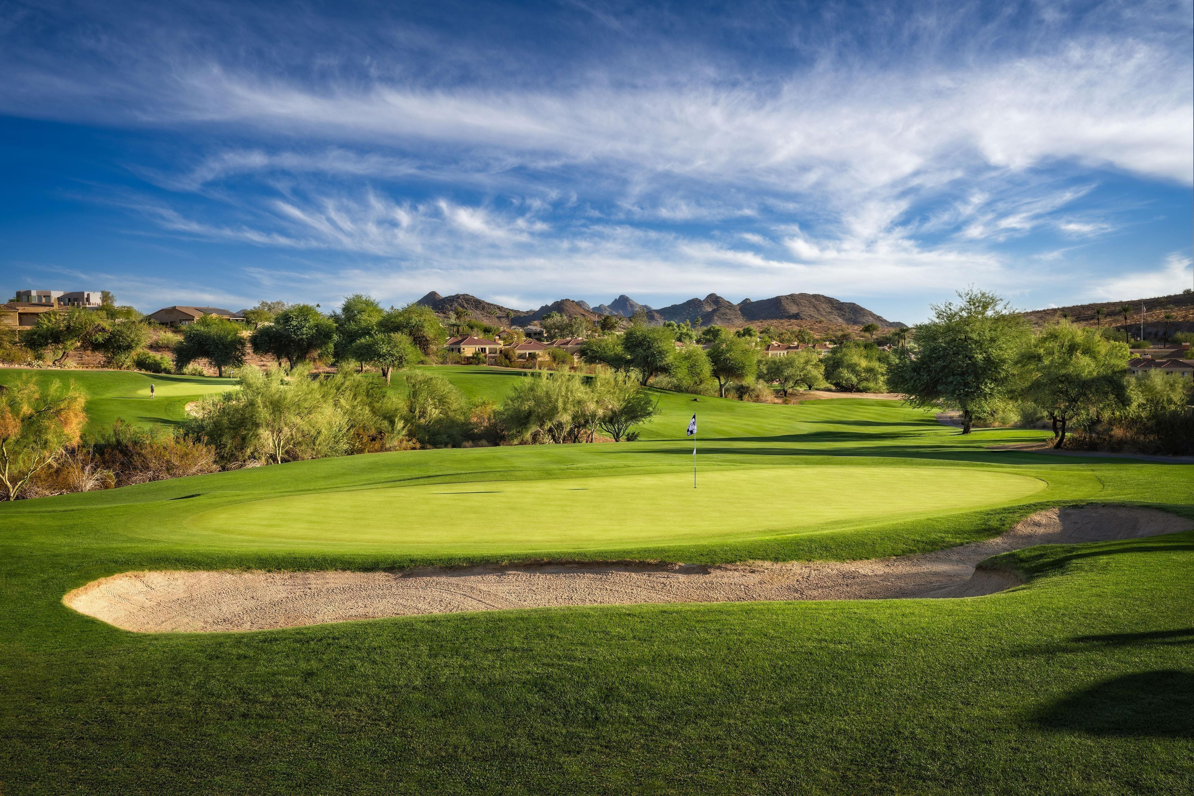 A golf course with a clear sky, green grass, and distant mountains.