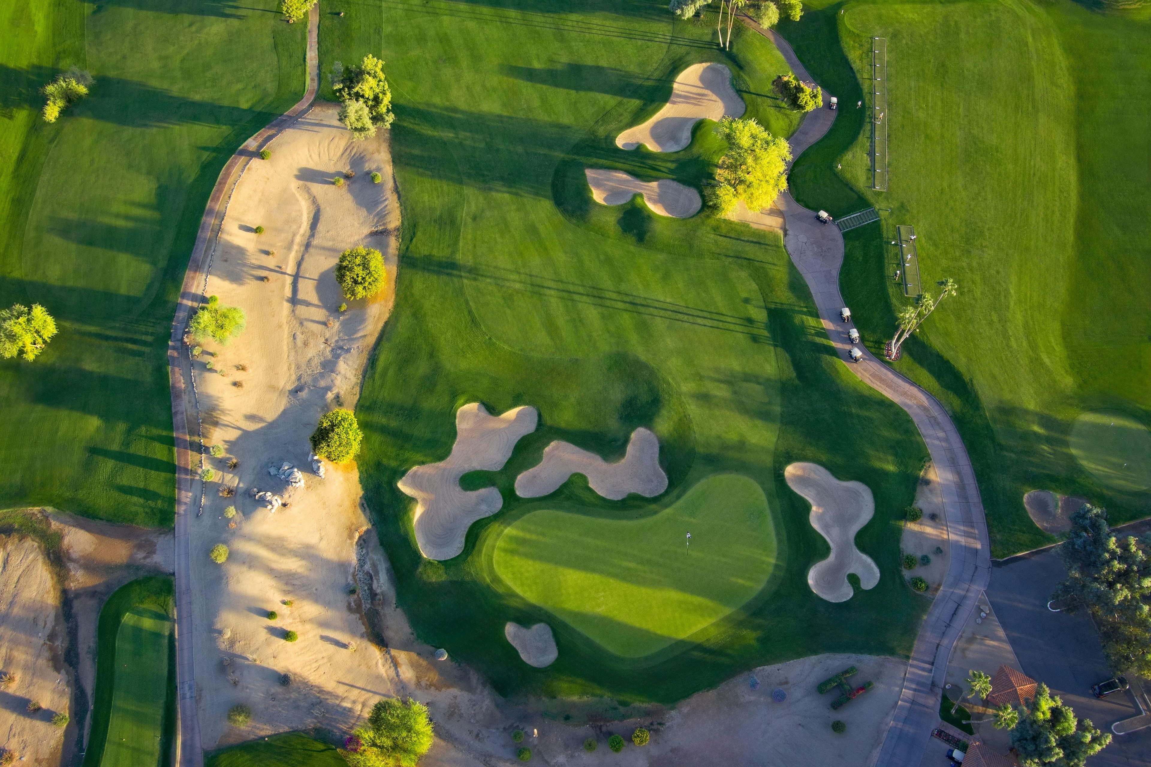 An aerial view of a golf course with sand bunkers, a putting green, and a road.