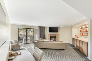 A modern living room with a sofa, a flat-screen TV, a fireplace, and a kitchen area with wooden cabinets.