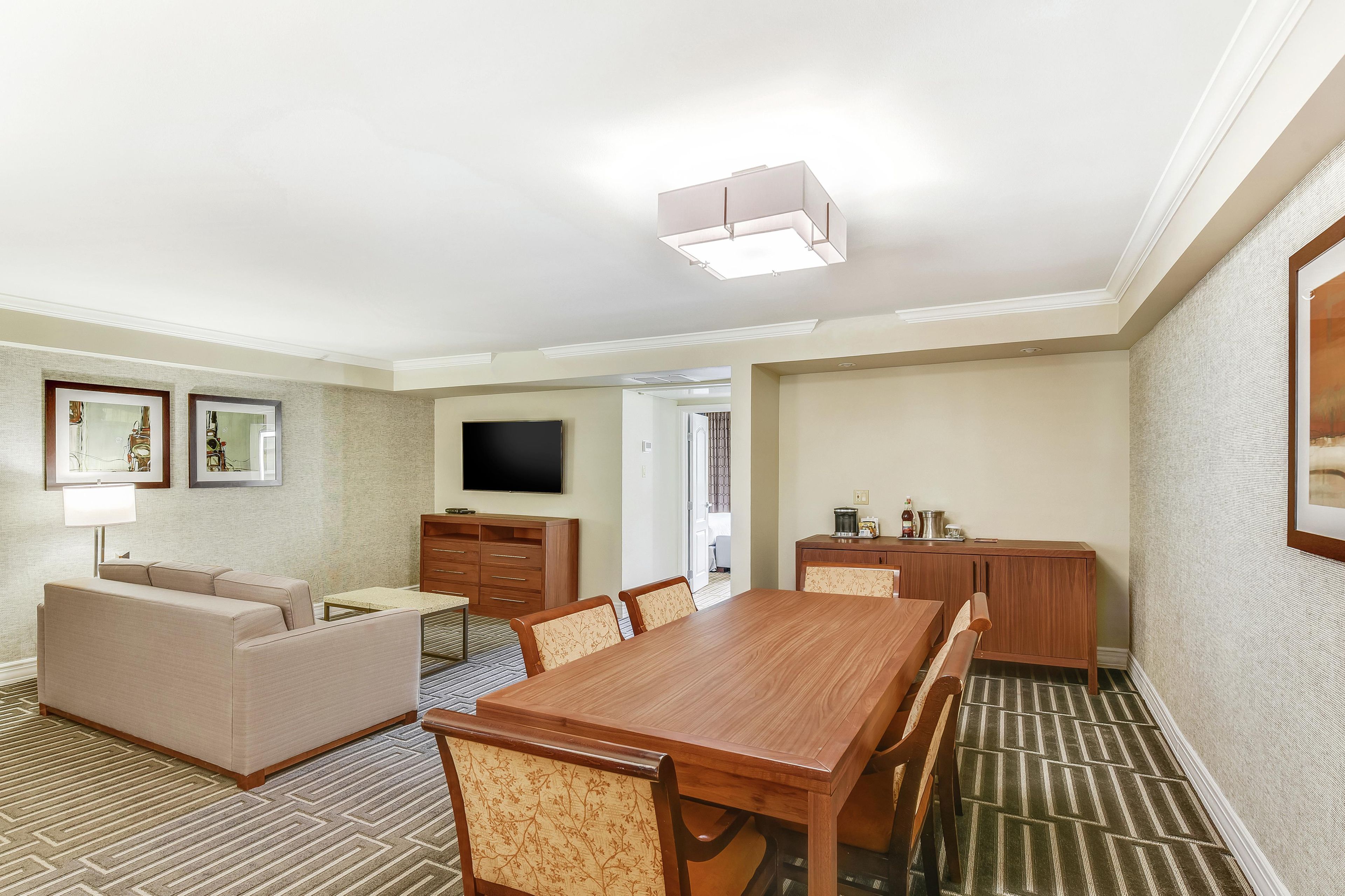 A hotel room with a dining area, a sofa, a TV, and a wooden cabinet.