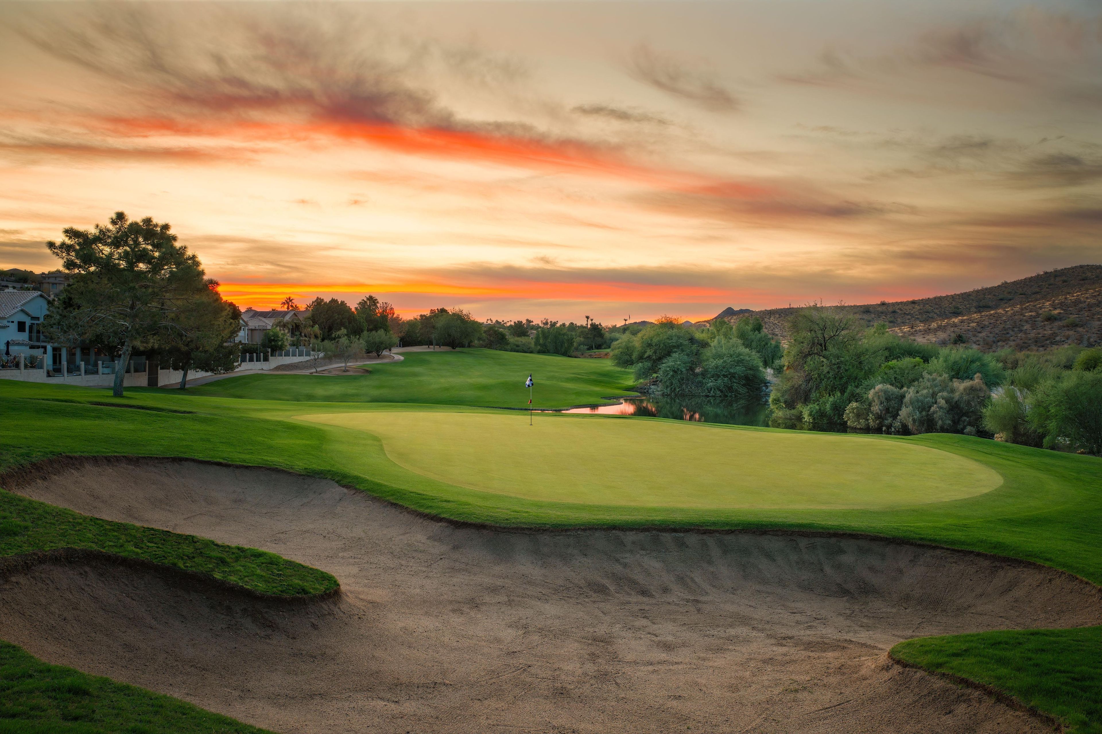 A golf course with a flagstick, sand bunkers, and a clubhouse in the background.