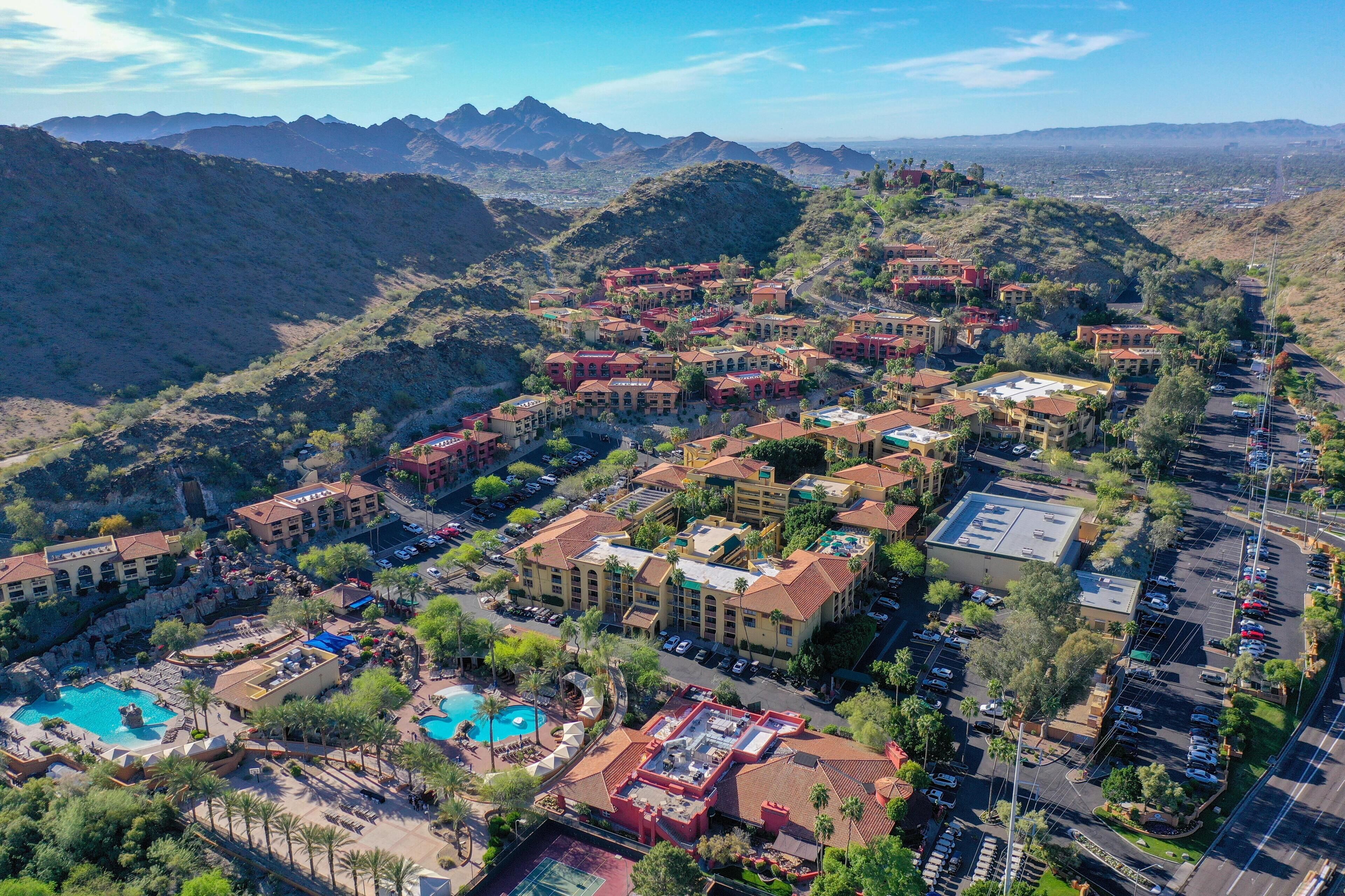 Vista aérea de un resort con varias construcciones, una piscina y montañas al fondo.