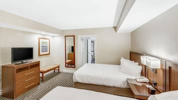 Habitación de hotel con cama, televisor, escritorio, espejo y puerta que da a un balcón.