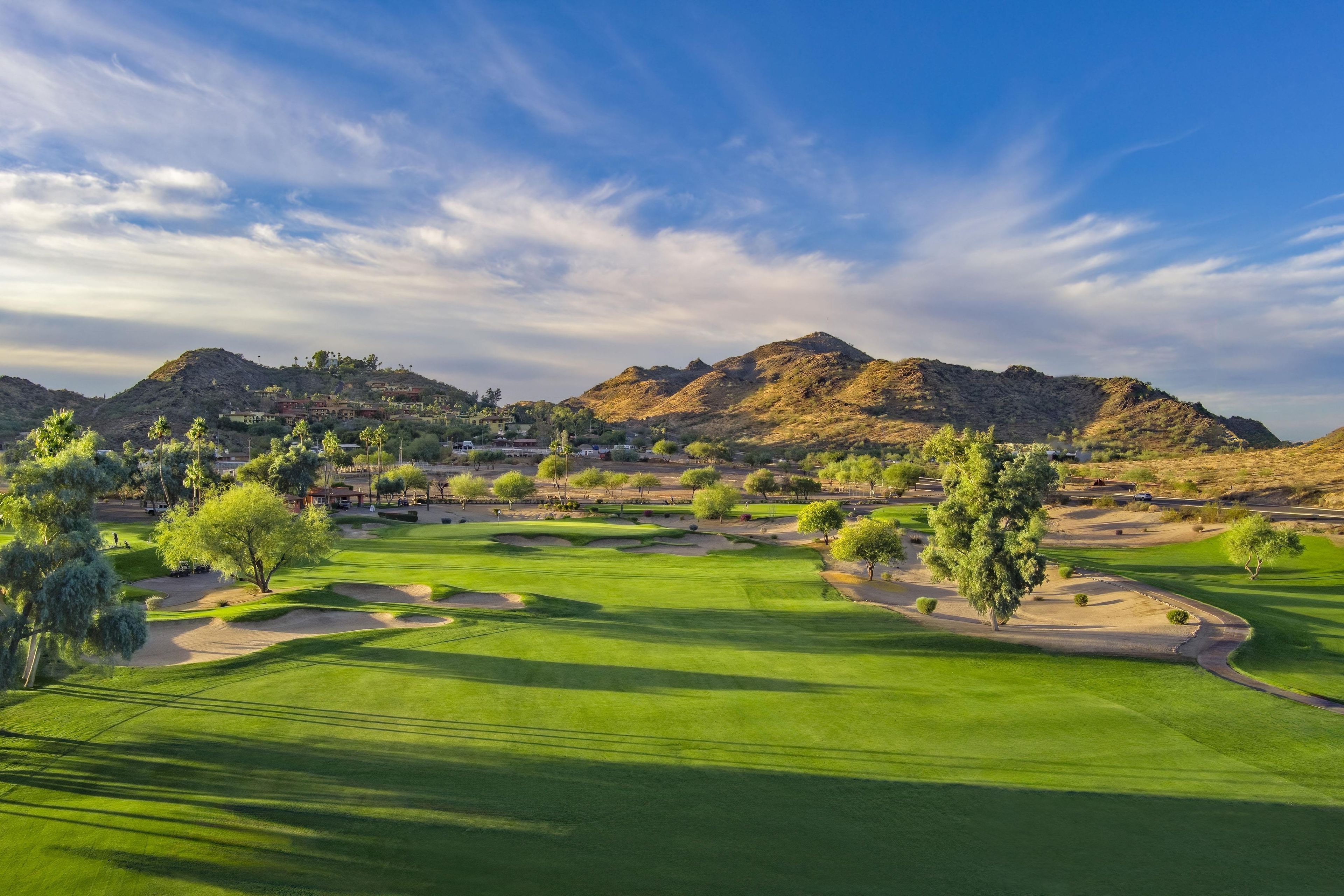 Un campo de golf con búnkeres de arena, árboles y montañas al fondo.