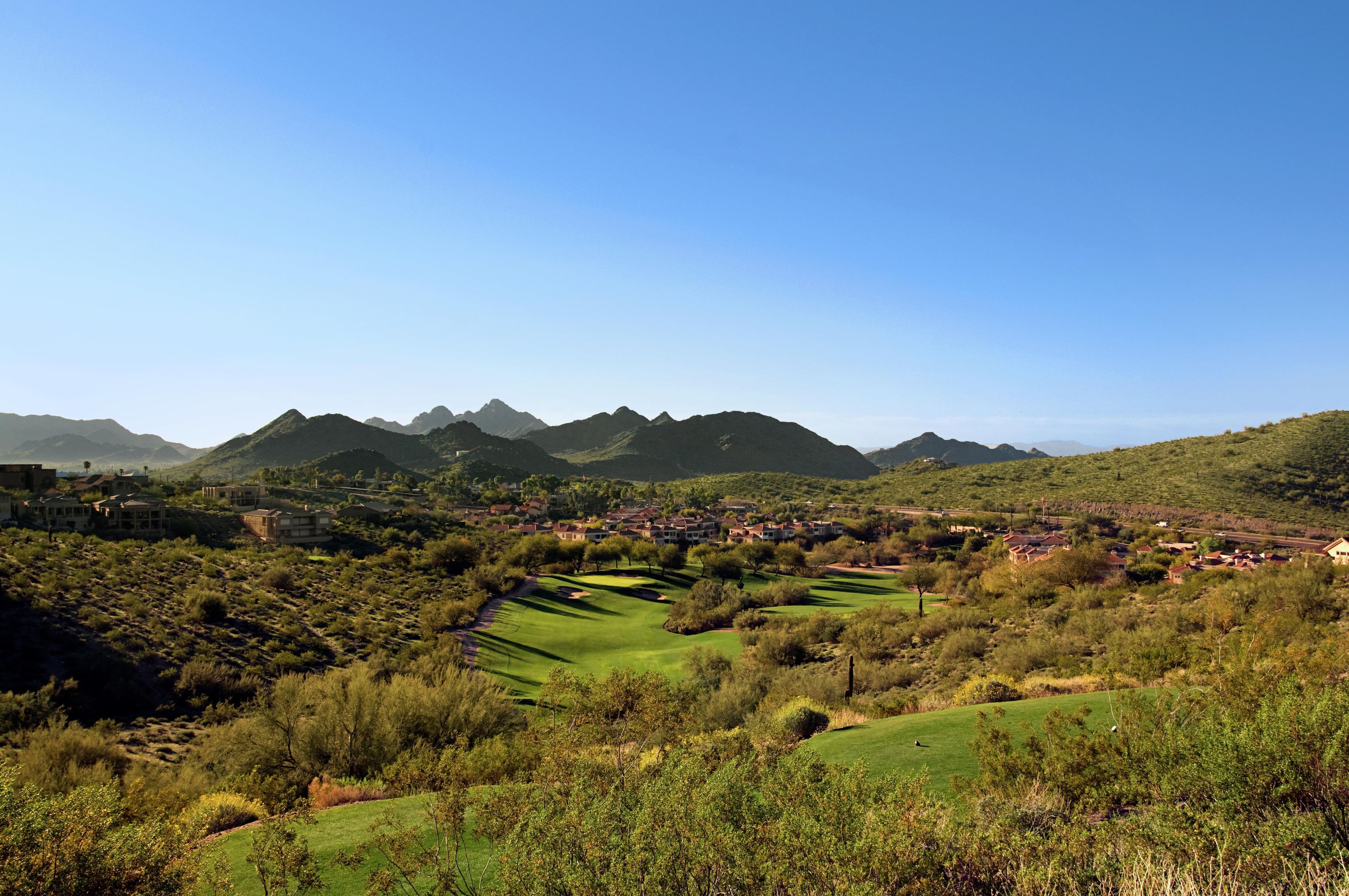 A golf course with a mountainous backdrop and residential buildings.