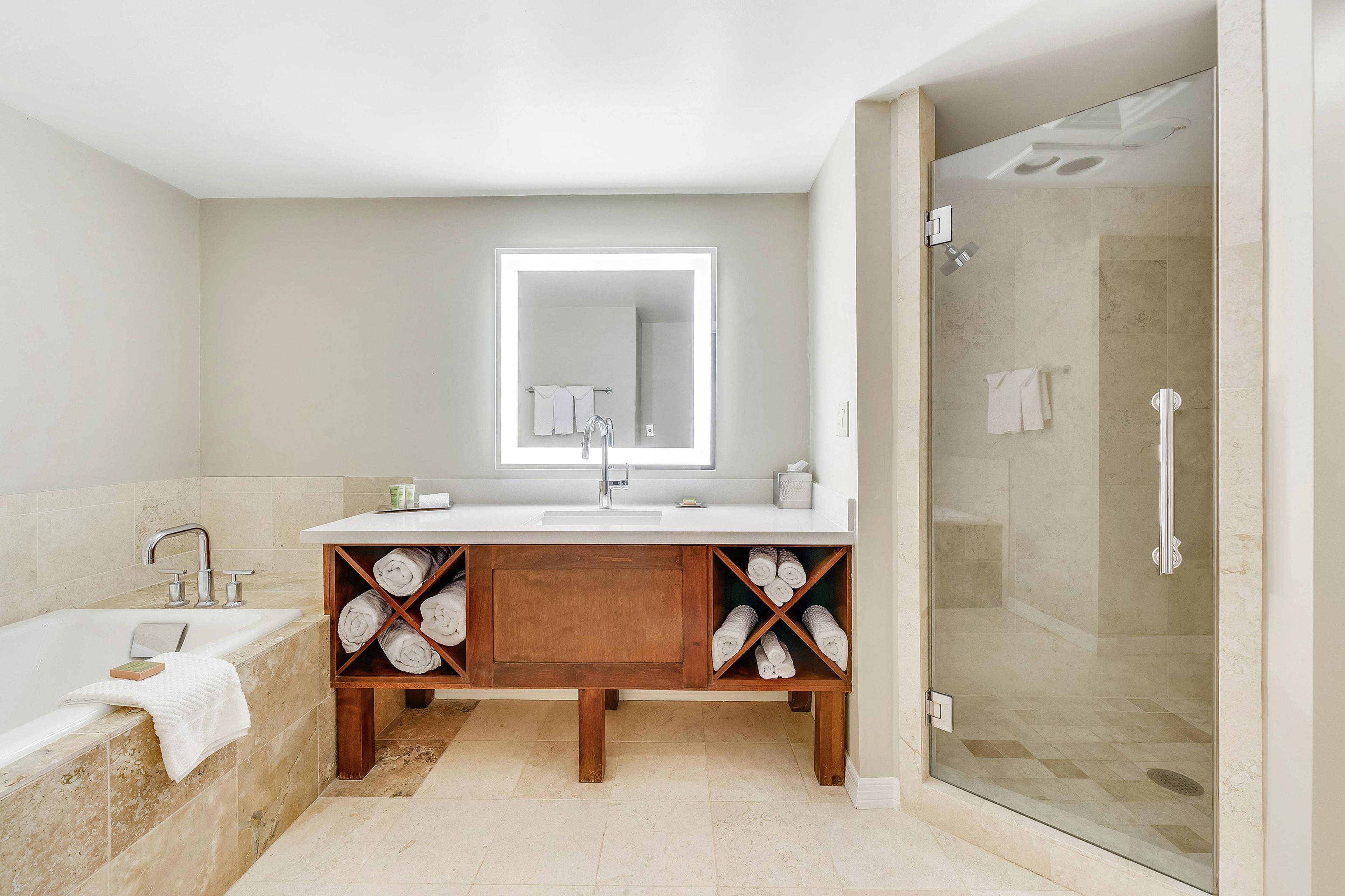 A modern bathroom with a bathtub, a glass-enclosed shower, a vanity with a mirror, and shelves with towels.