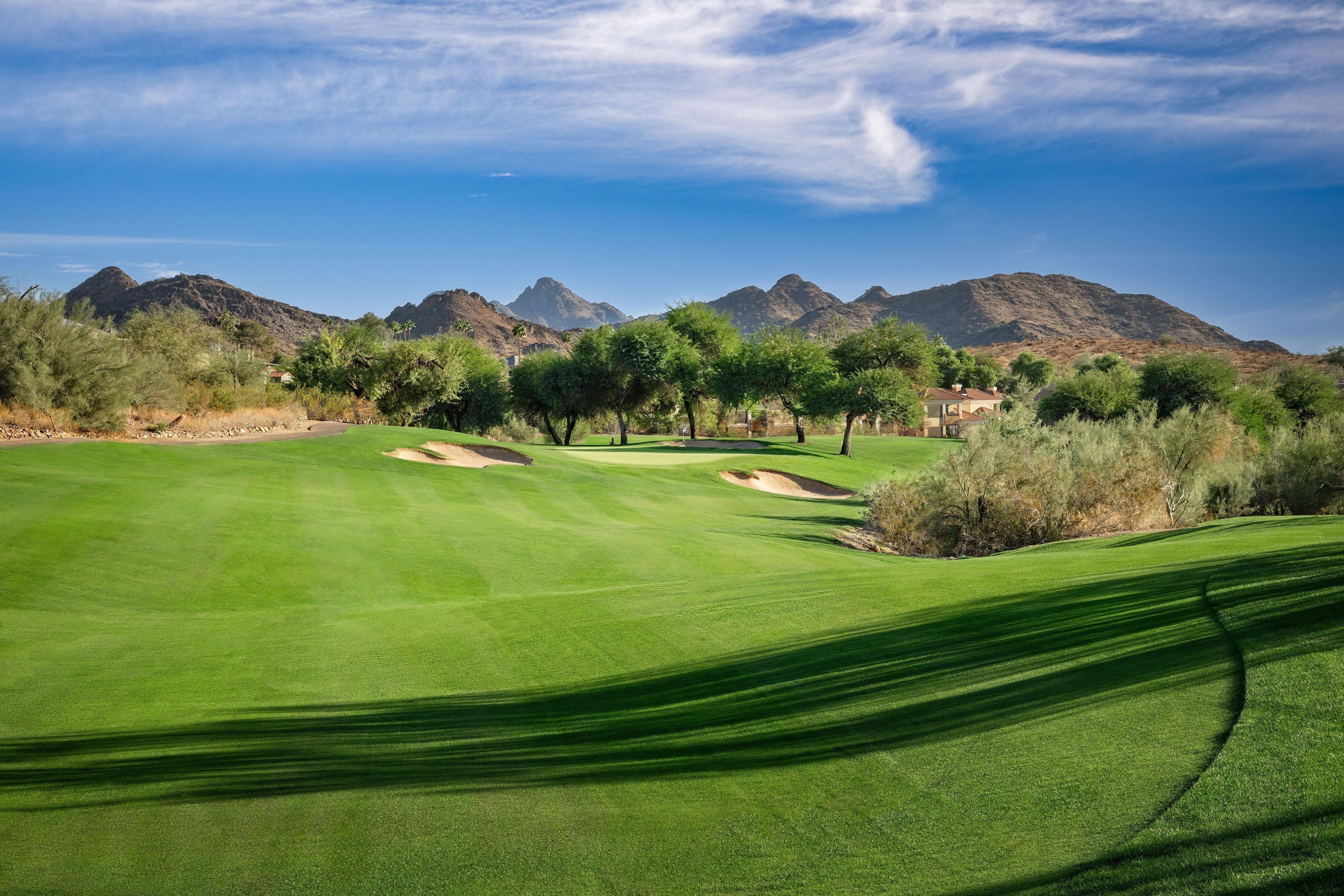 A golf course with a clear sky, mountains in the background, and a well-maintained green.