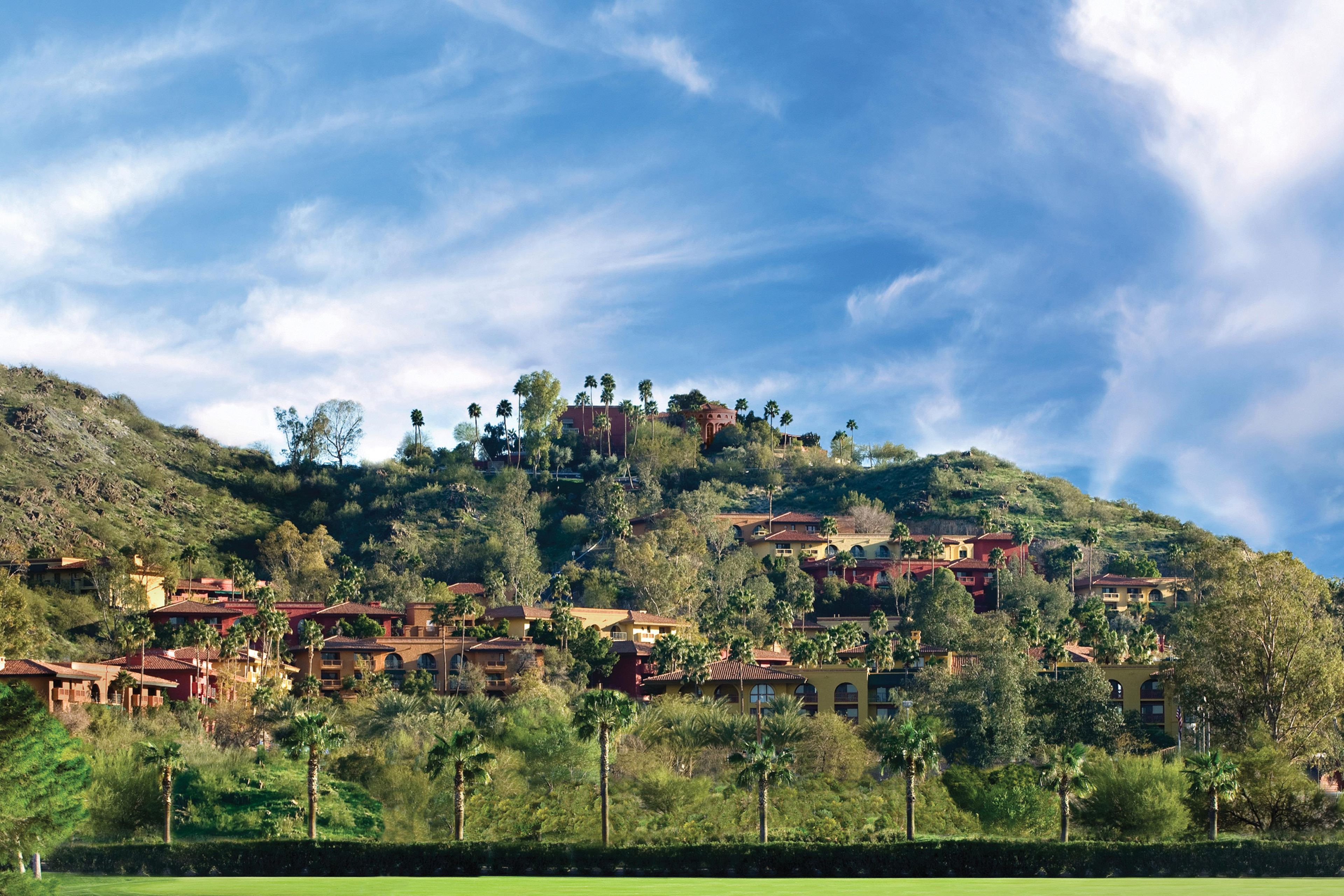 A hillside residential area with multiple houses, some with red roofs, surrounded by greenery and trees.