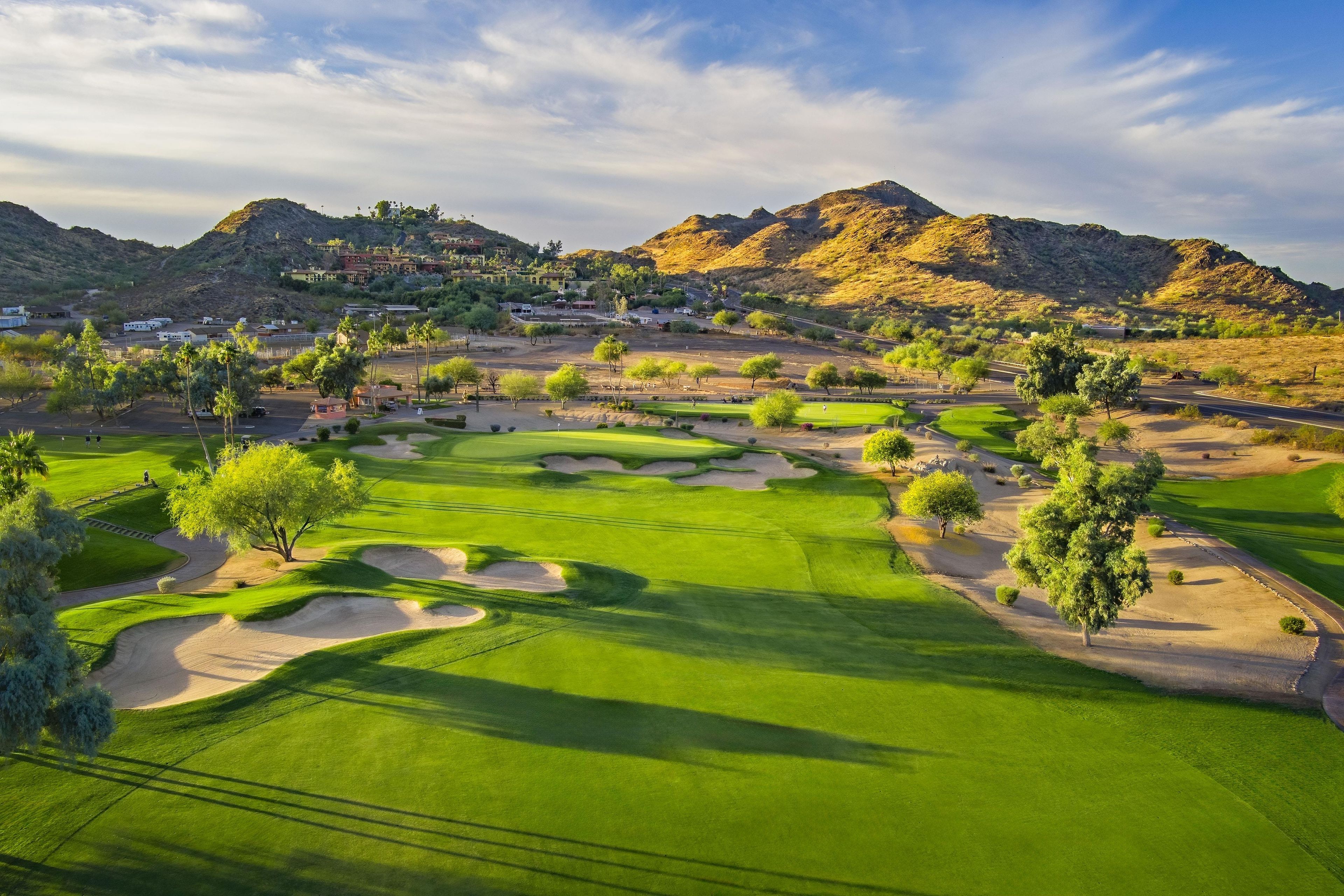 Un parcours de golf avec des bunkers de sable, des arbres et une chaîne de montagnes en arrière-plan.