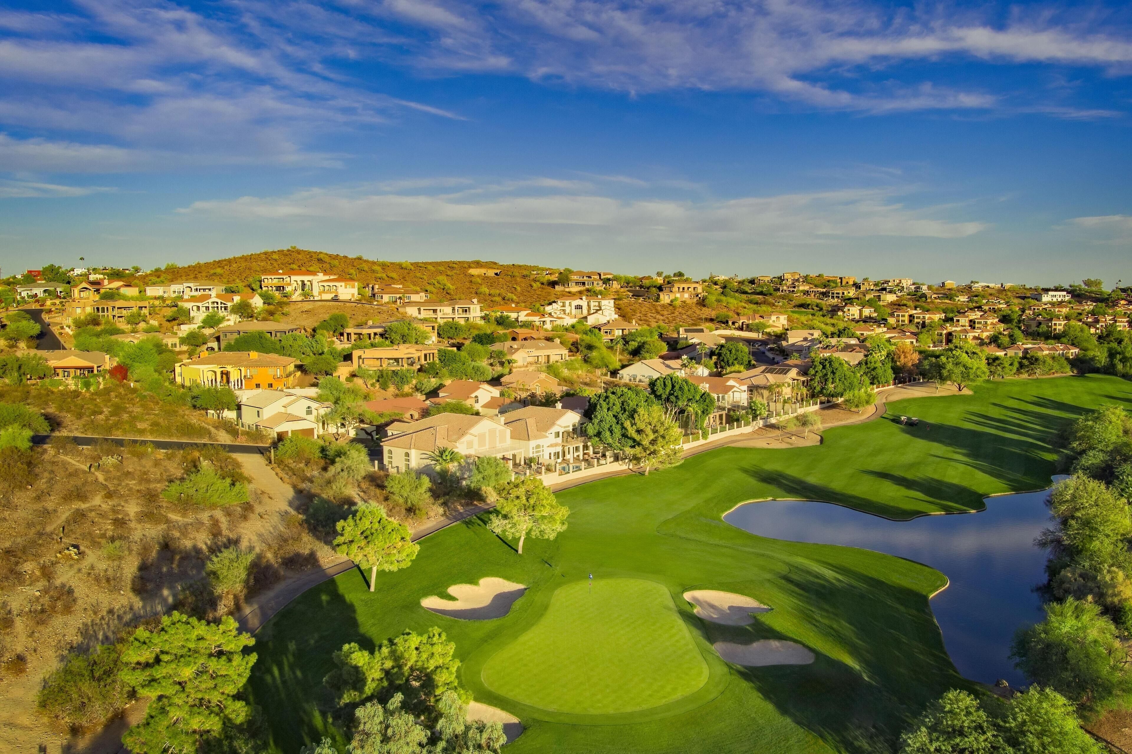 A golf course with a pond, surrounded by residential buildings and a hilly landscape.