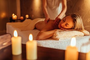A spa setting with a massage table, candles, and a person providing a massage.