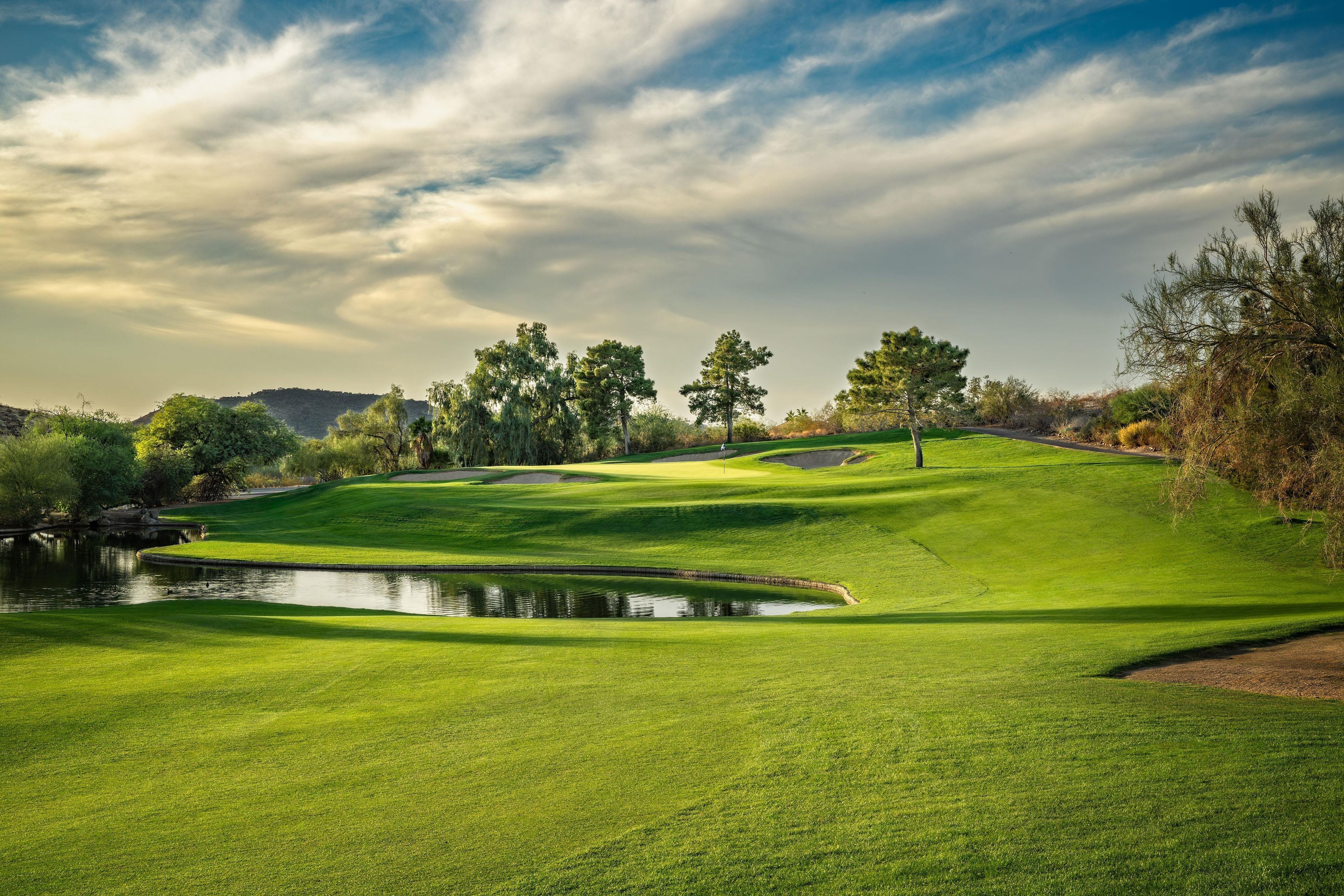 A well-maintained golf course with a pond, trees, and a hilly landscape.