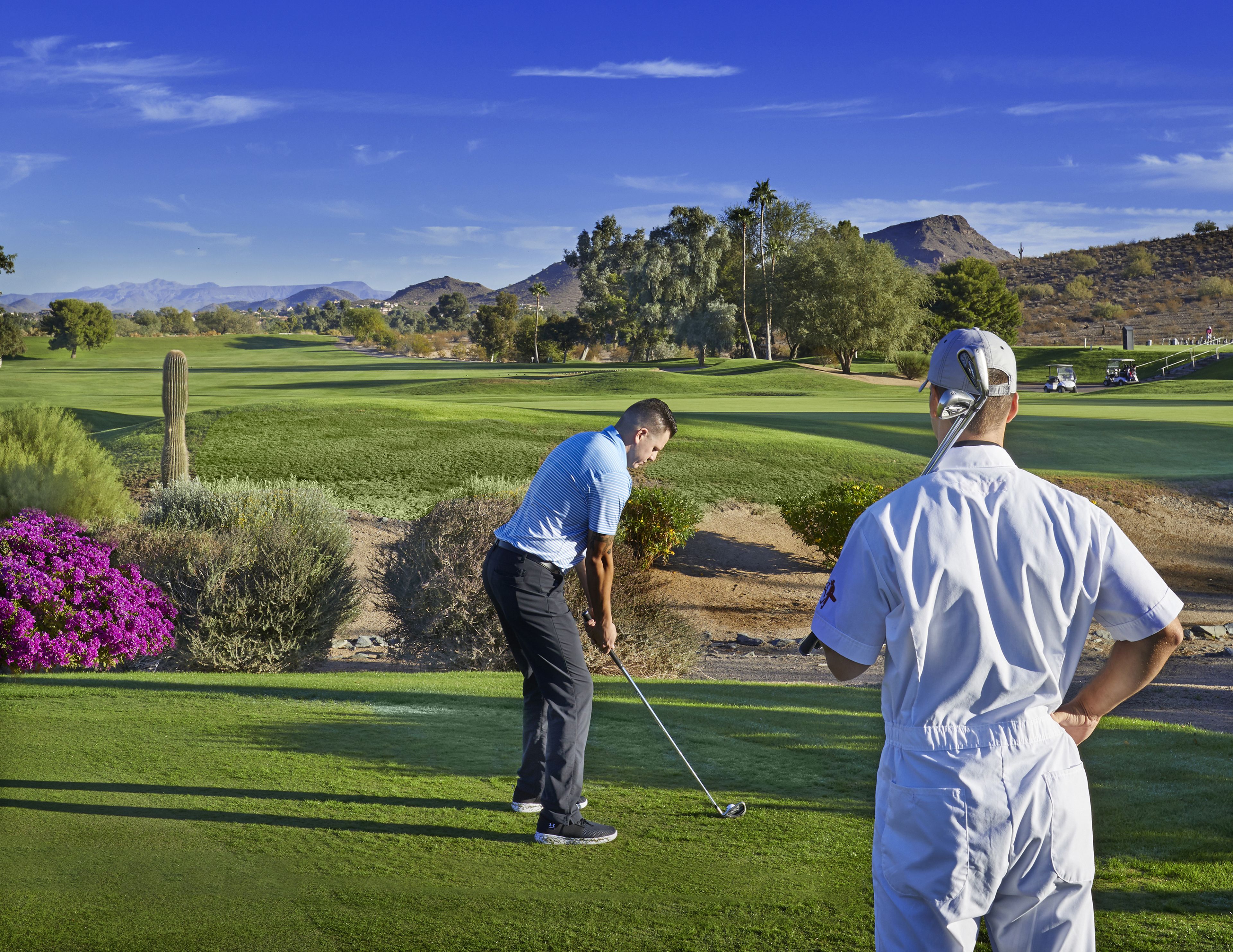 A golf course with a clear sky, green grass, and distant mountains.