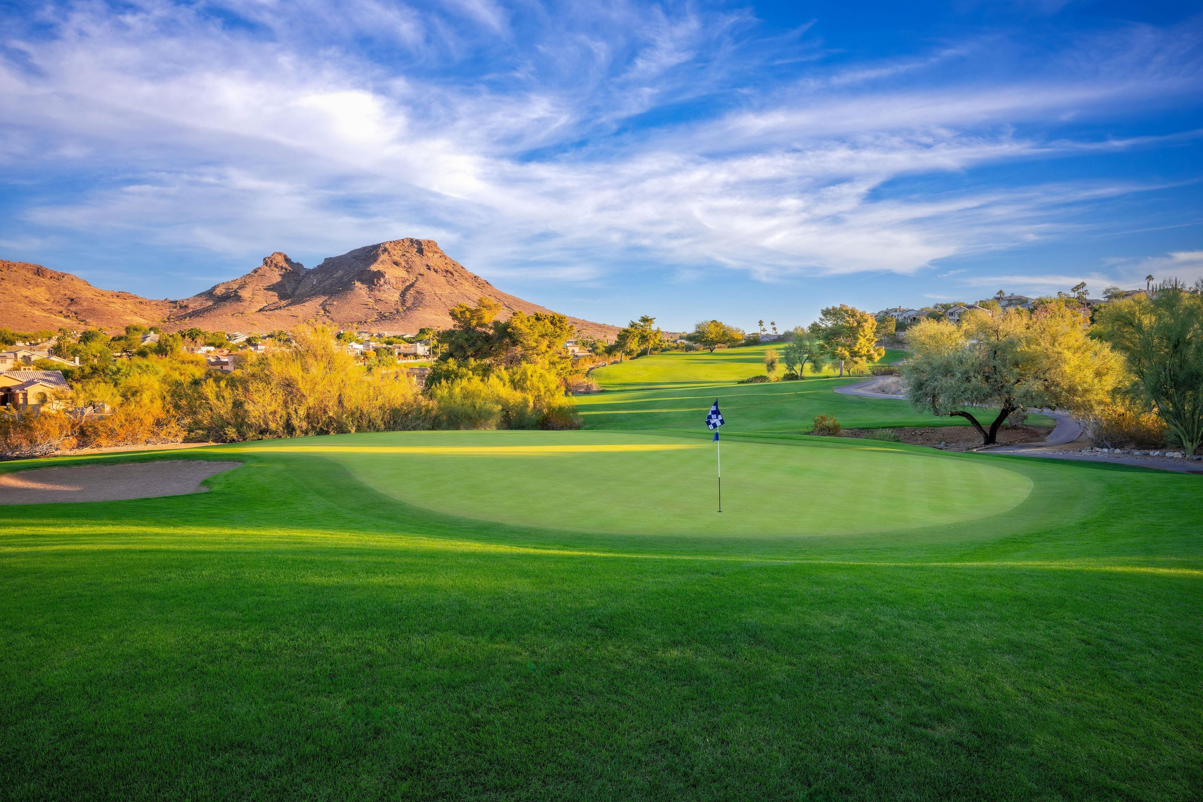 A golf course with a flagstick, a mountain in the background, and a clear sky.