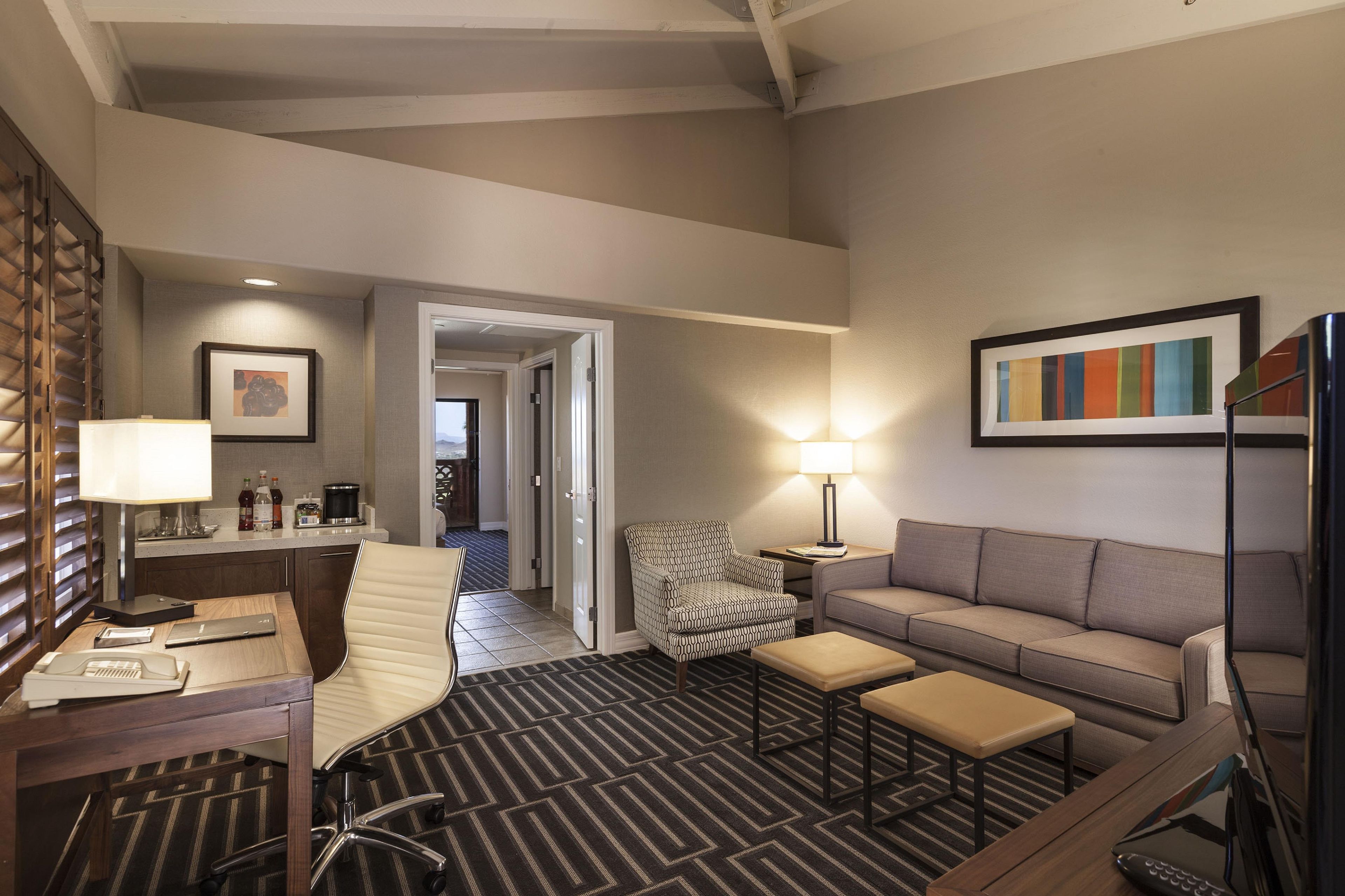 Una habitación de hotel con escritorio, silla, sofá y alfombra estampada.