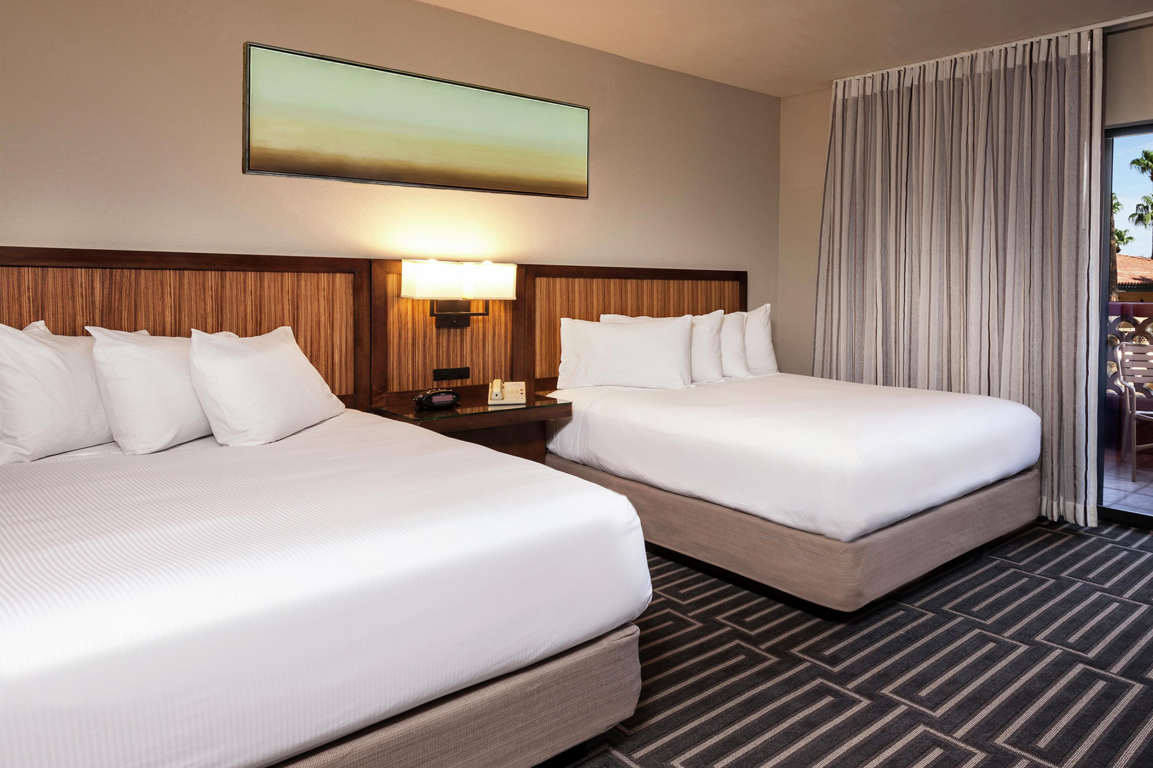 Una habitación de hotel con dos camas, una mesita de noche, una lámpara y un ventanal con cortinas.