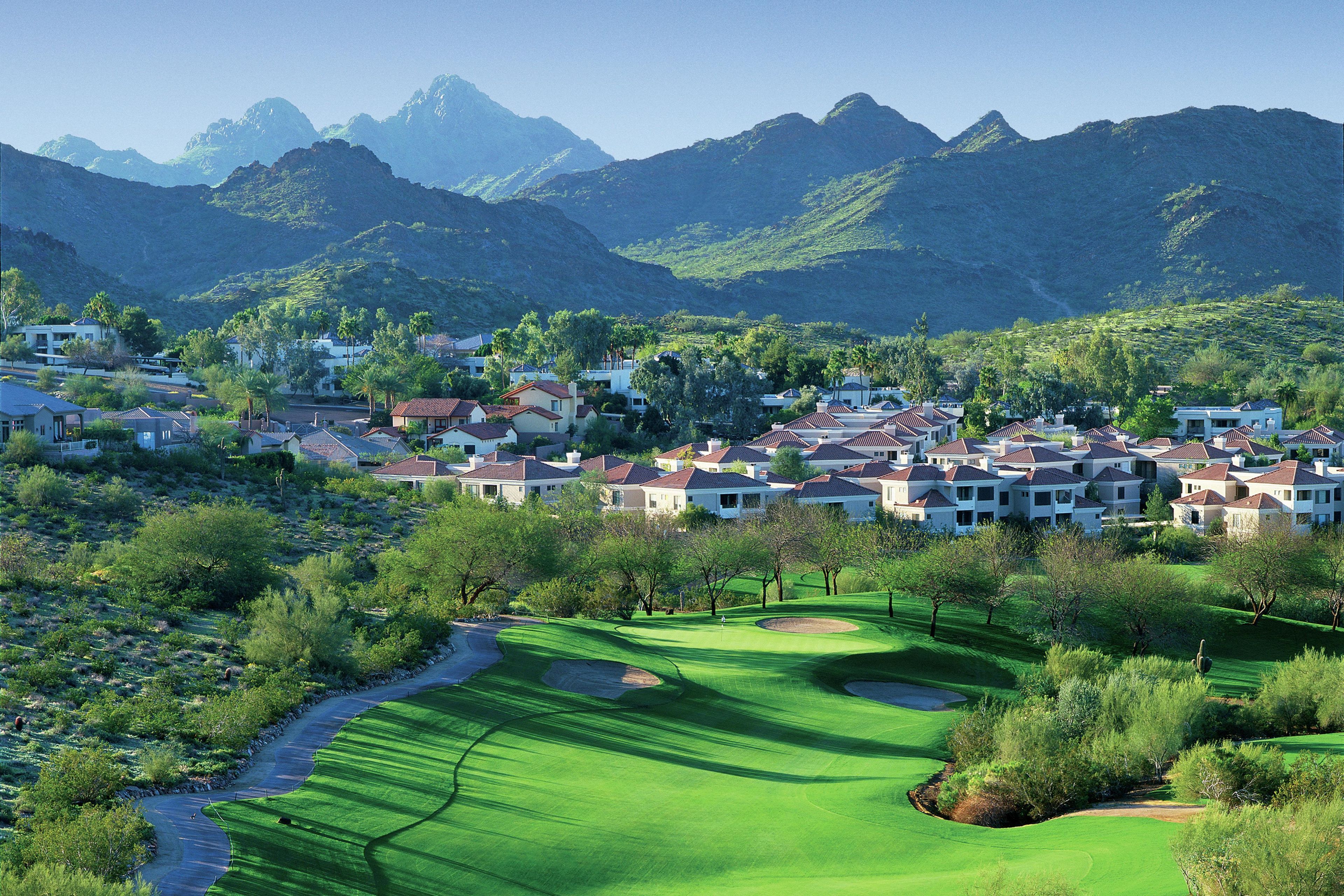 A residential area with houses, a golf course, and mountains in the background.