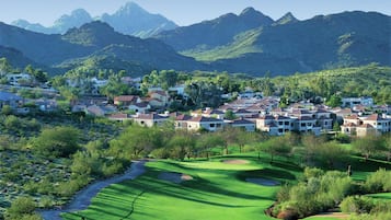 A residential area with houses, a golf course, and mountains in the background.