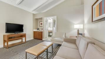 Ein Wohnzimmer mit Fernseher, Sofa, Bank, gemustertem Teppich und einer Tür zu einem Badezimmer.