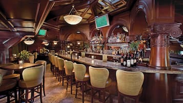 A bar area with multiple seating options, a variety of bottles, and a television screen.