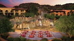 A resort with outdoor dining, a waterfall, and buildings with balconies.