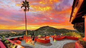A rooftop terrace with outdoor seating, a palm tree, and a view of a mountain range.