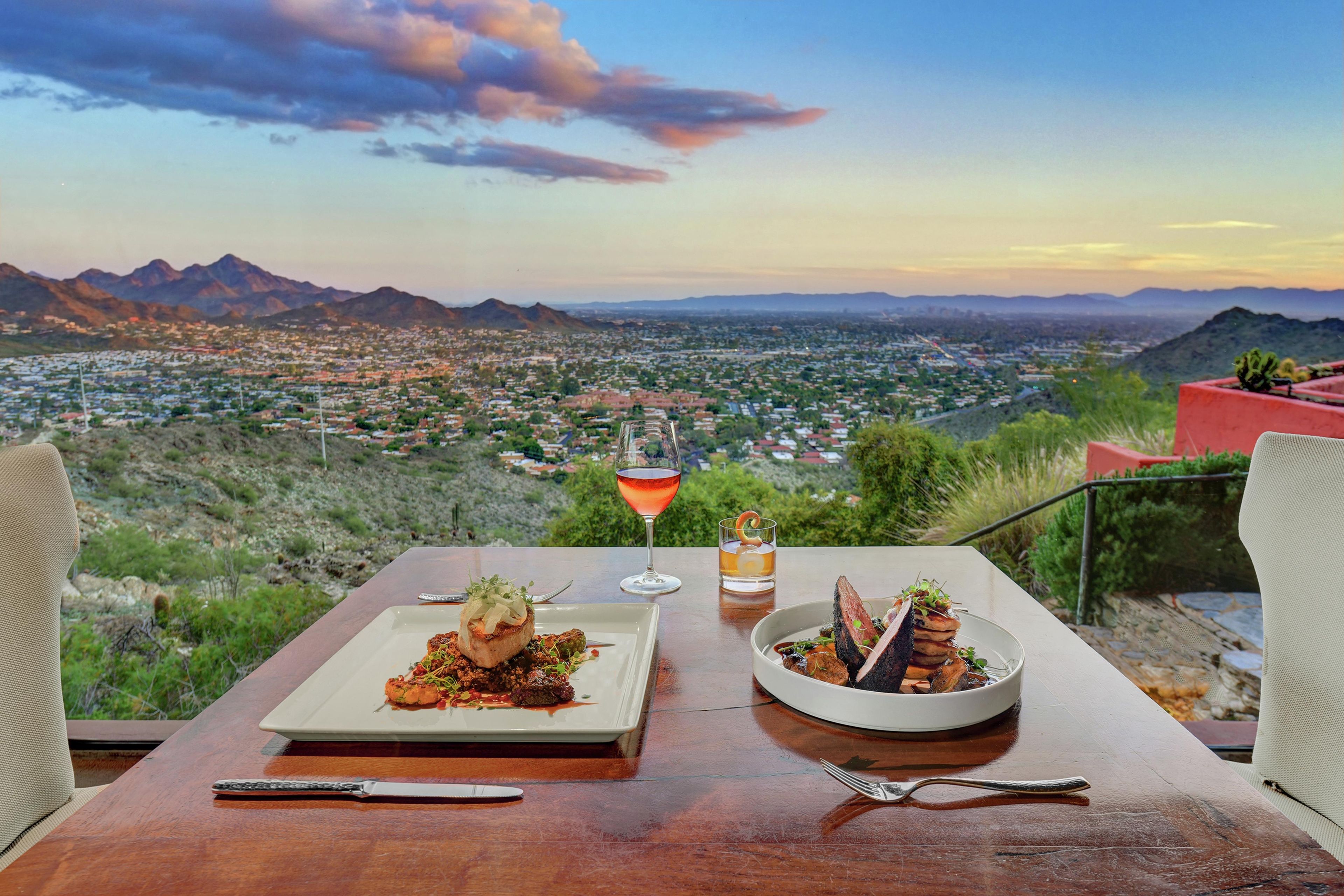 Una mesa con dos platos y una bebida, con vistas a un paisaje urbano y montañas.